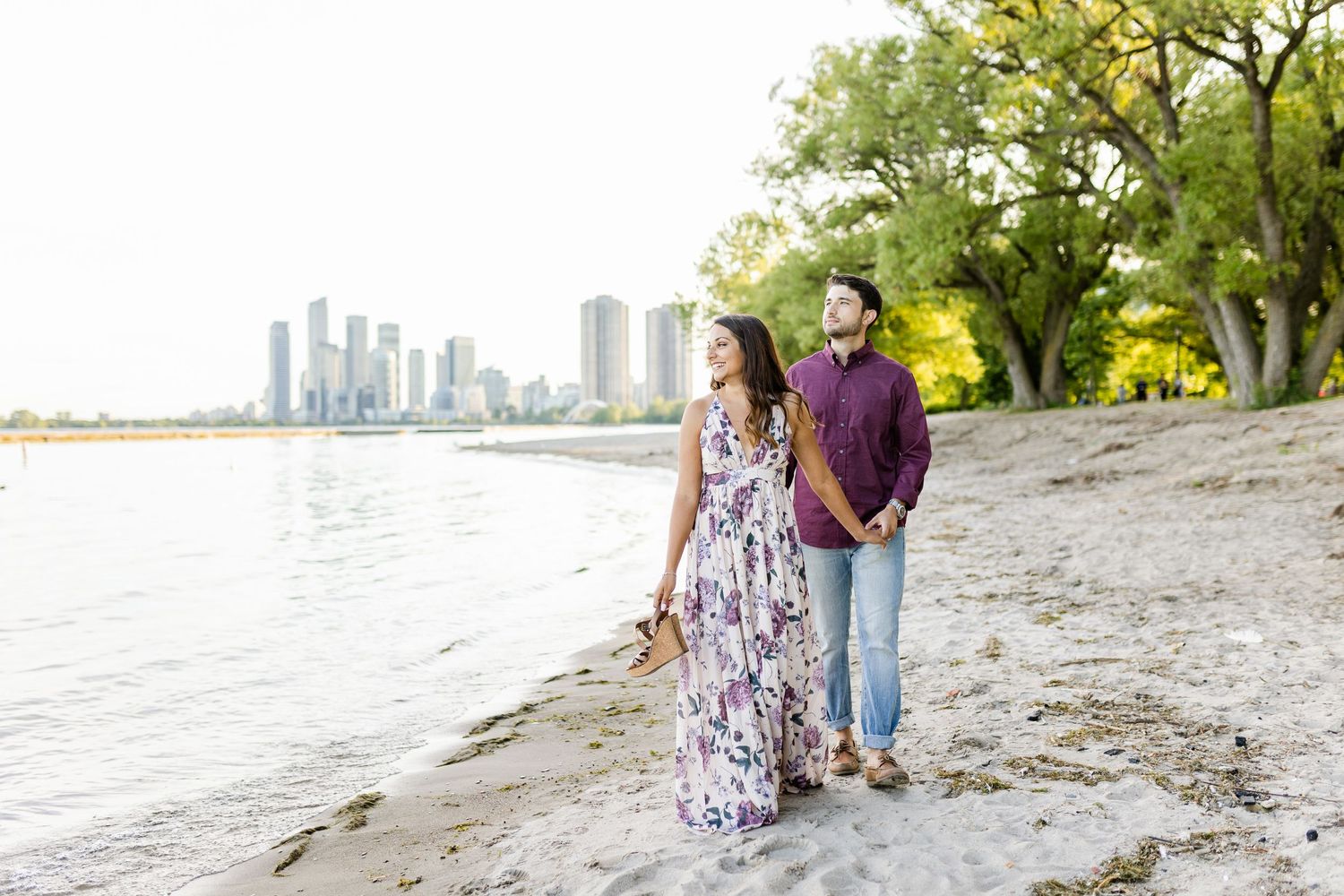A couple strolling along the beach with city skyline in the background.