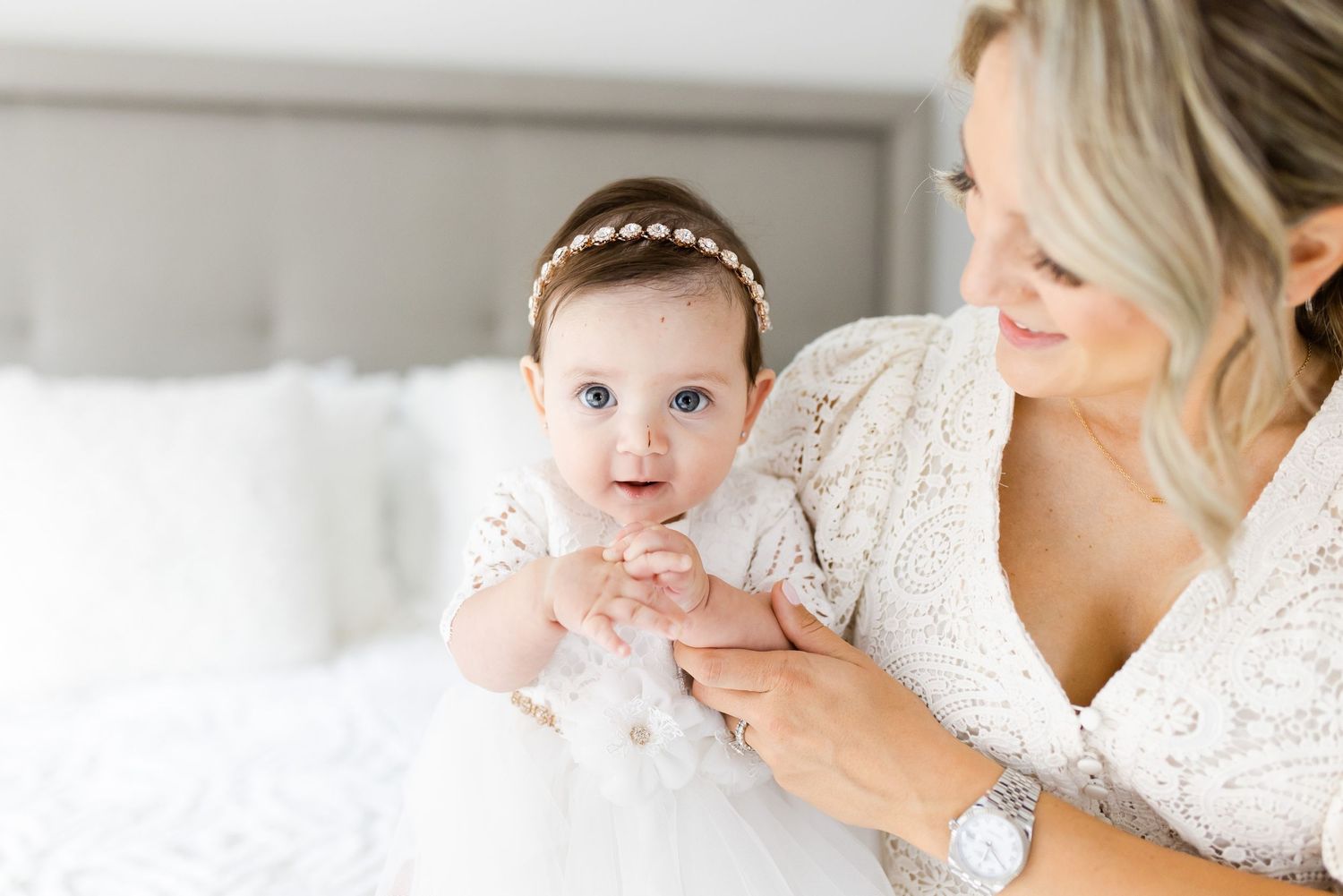 Baby in white christening gown held by woman in lace dress.