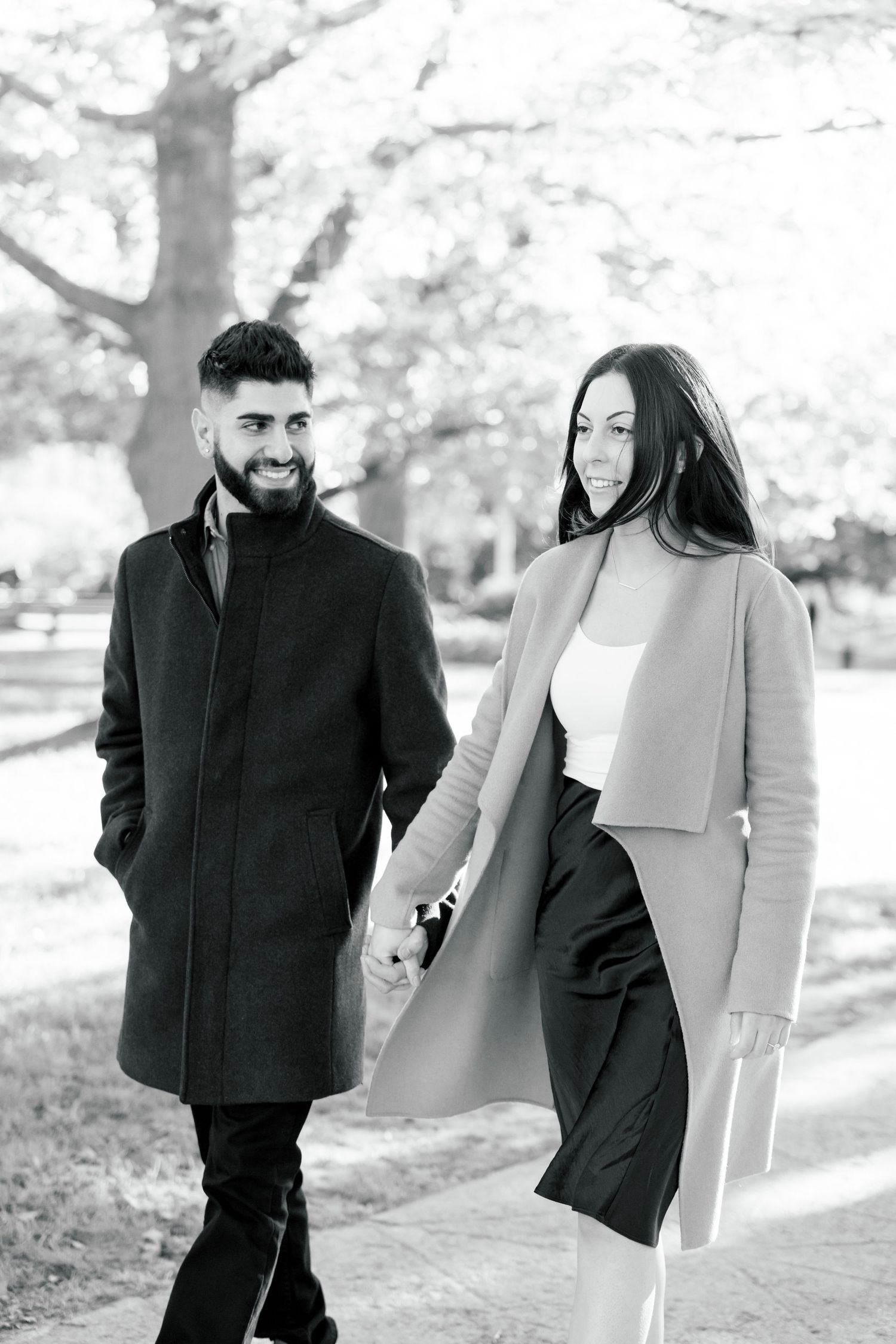A stylish couple in wool coats shares a tender moment while walking through a park.