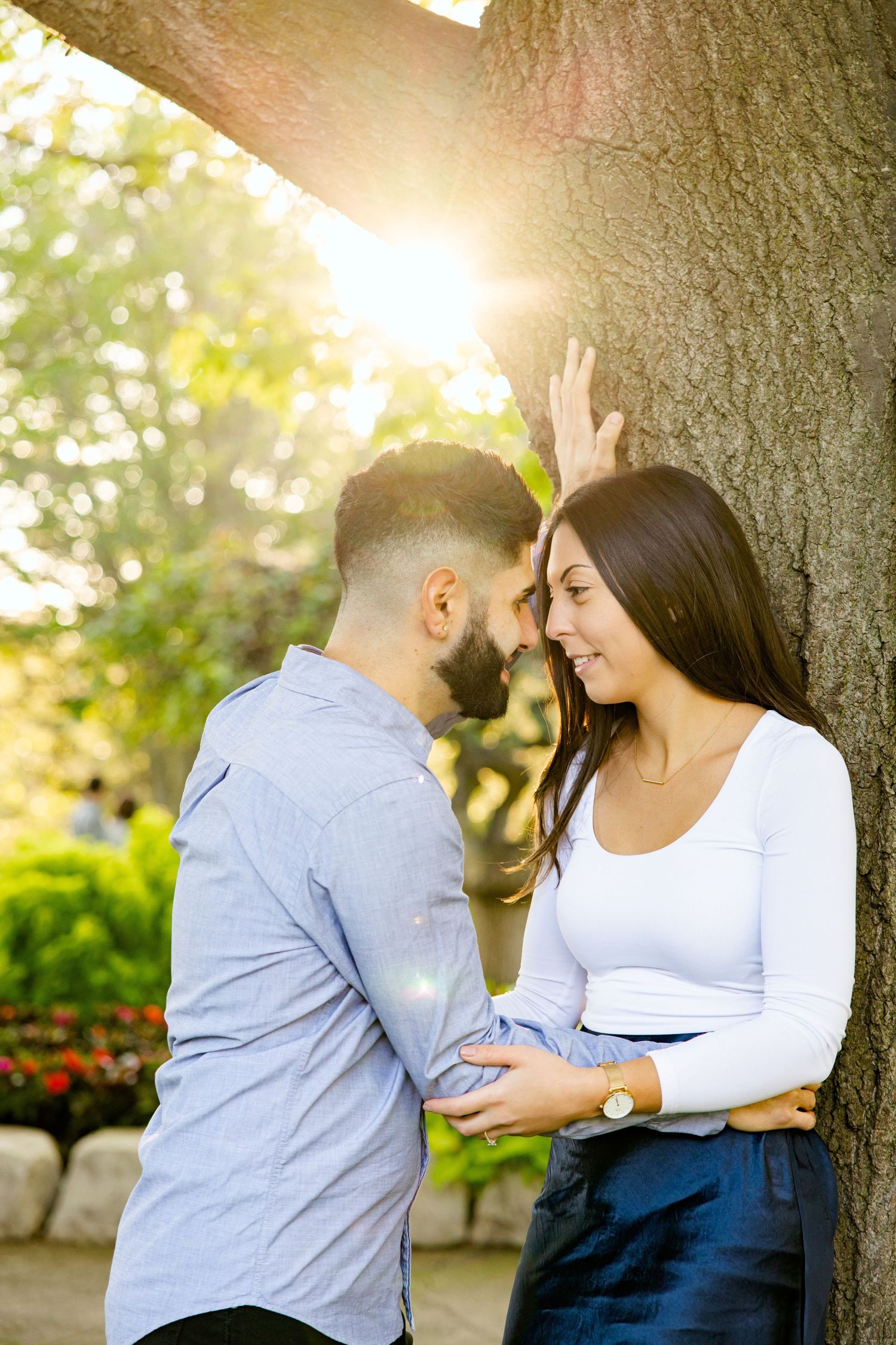 Romantic couple sharing tender moment against large tree trunk with sunburst.