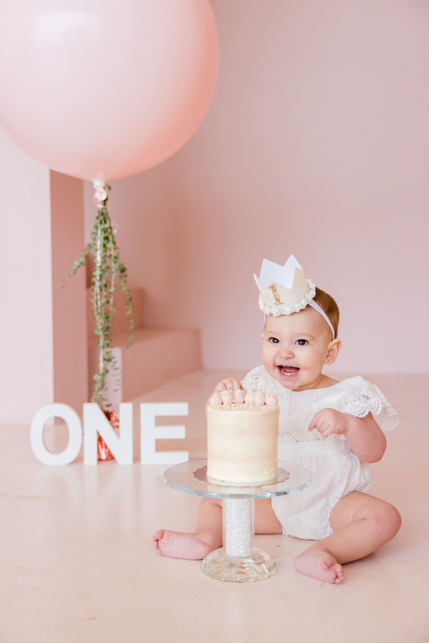 Joyful first birthday celebration setup with pink balloon, cake, and ONE letters in soft pink setting.