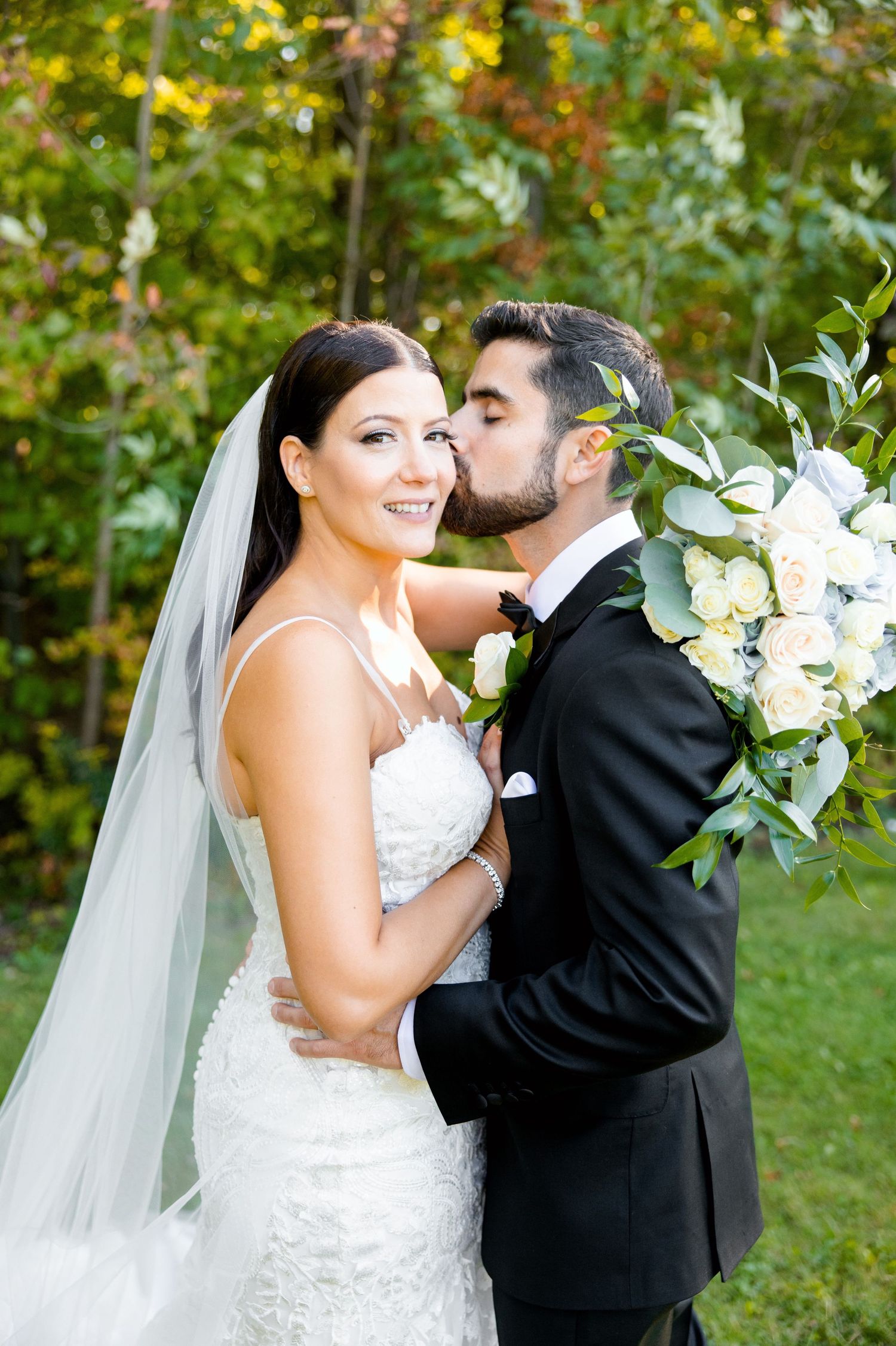 Intimate wedding portrait features couple sharing tender moment with white floral bouquet.