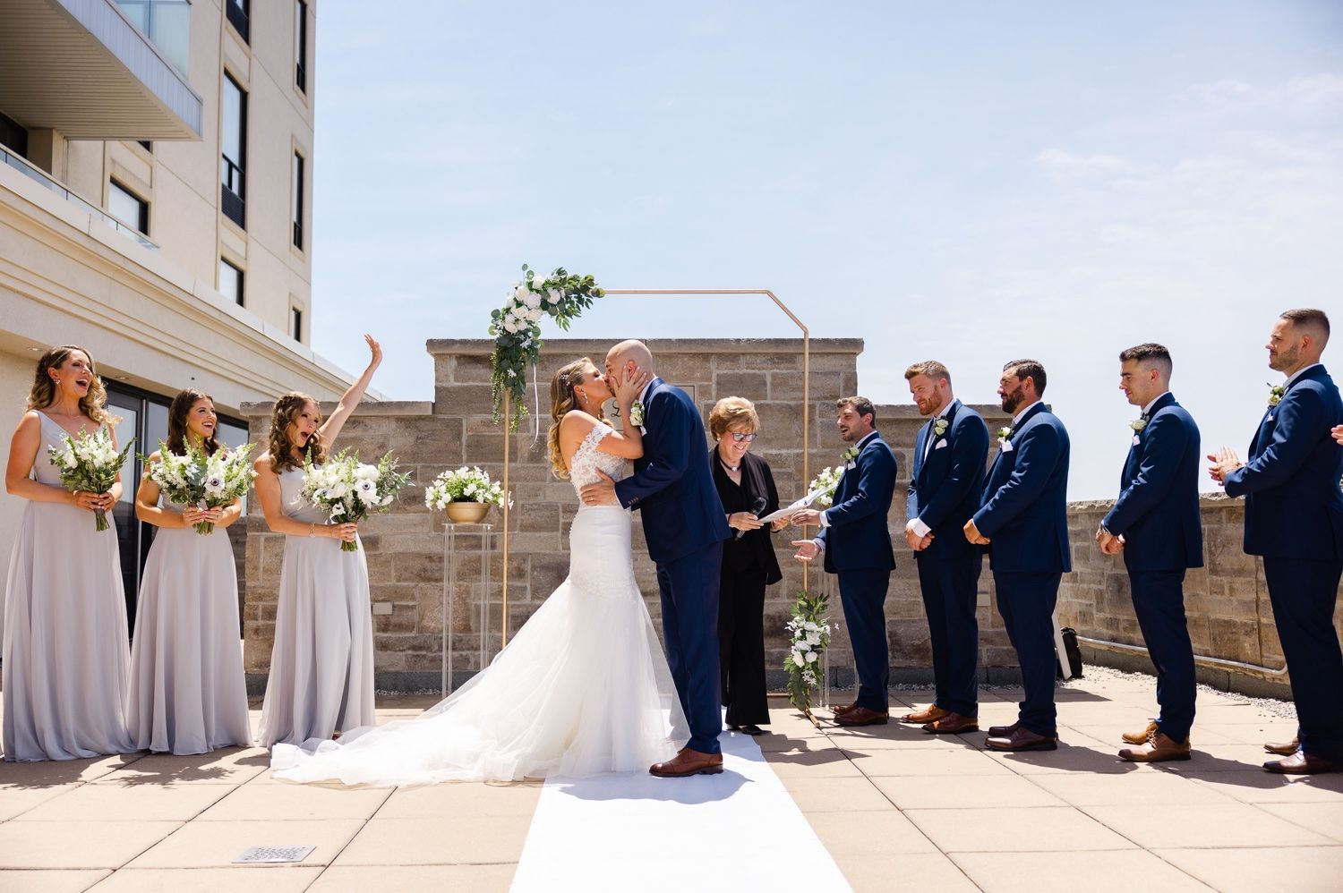 Full wedding party scene with bridesmaids in lavender and groomsmen in navy suits during an outdoor ceremony.