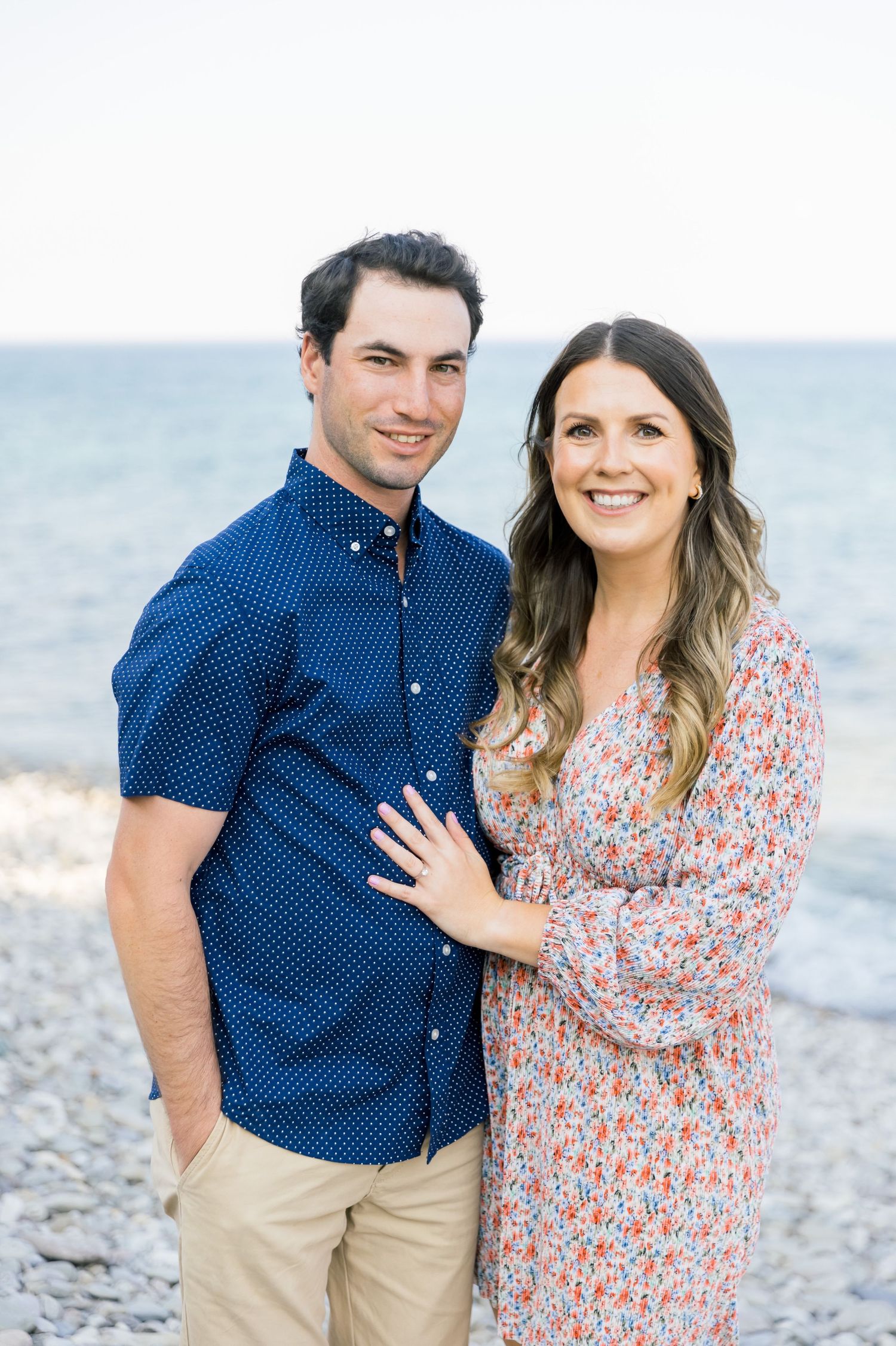 A couple in coordinated outfits poses together against an ocean backdrop on a bright day.