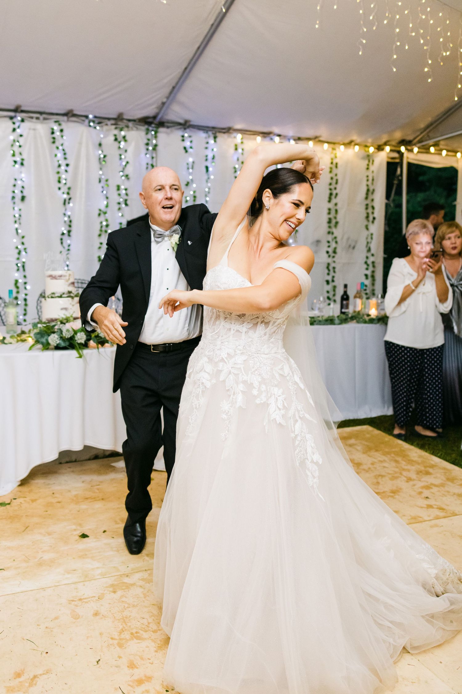 Dancing moment captured under tent with string lights and floral decorations at wedding reception.