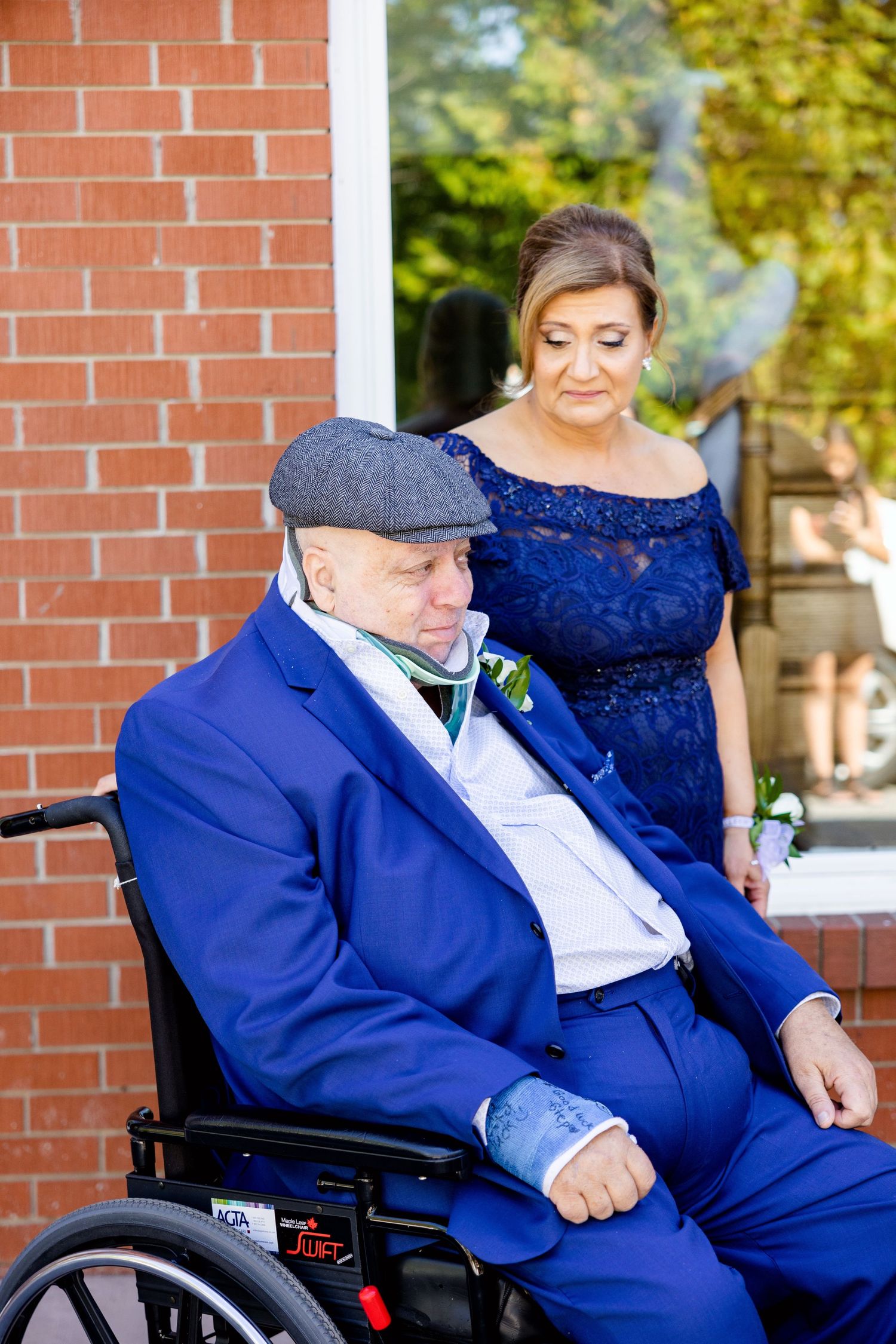 Touching outdoor portrait with gentleman in wheelchair wearing navy suit and flat cap.