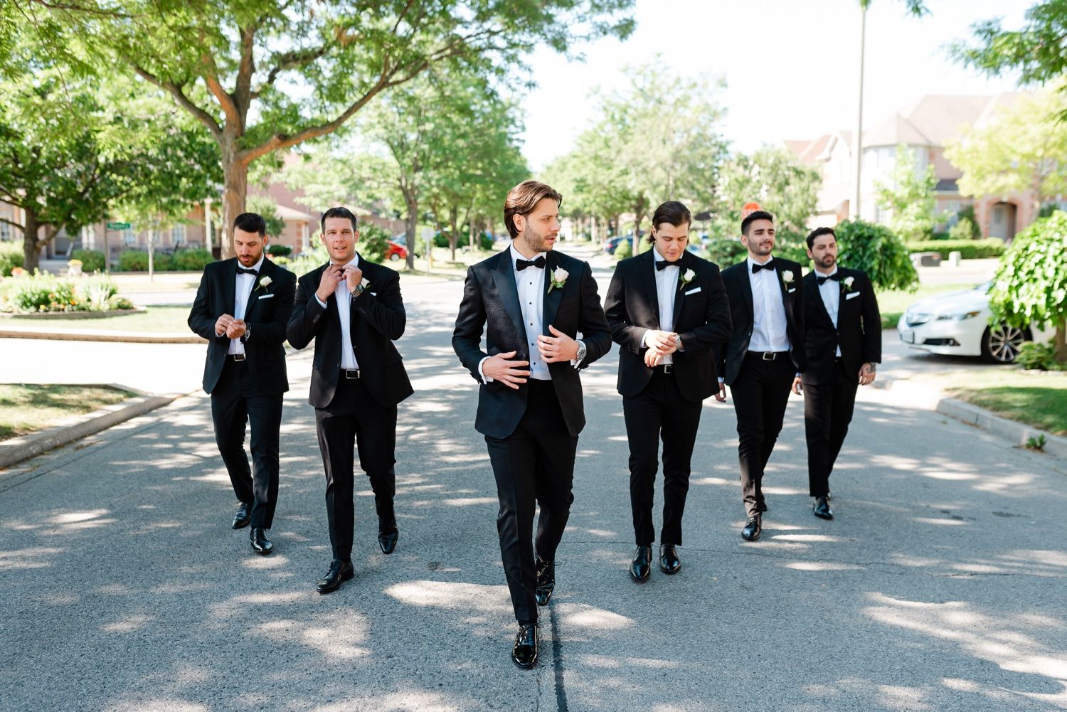 Group walking down street in formal black tuxedos during wedding day.