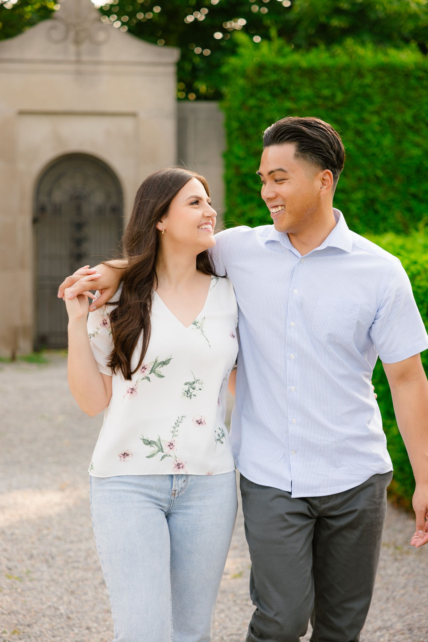 A happy couple shares joyful laughter while walking together in a manicured garden setting.