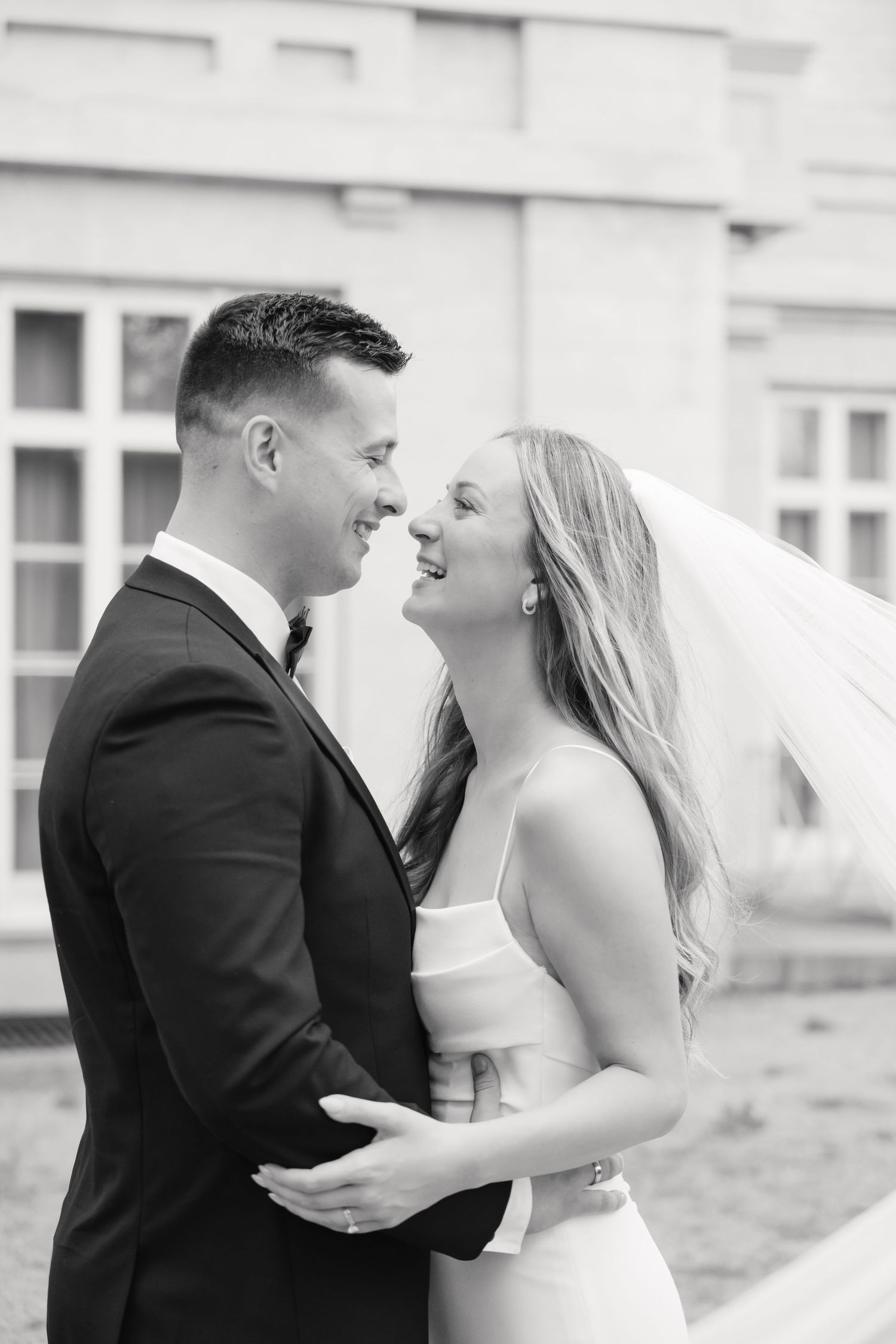 Black and white wedding portrait capturing a candid laughing moment between newlyweds.