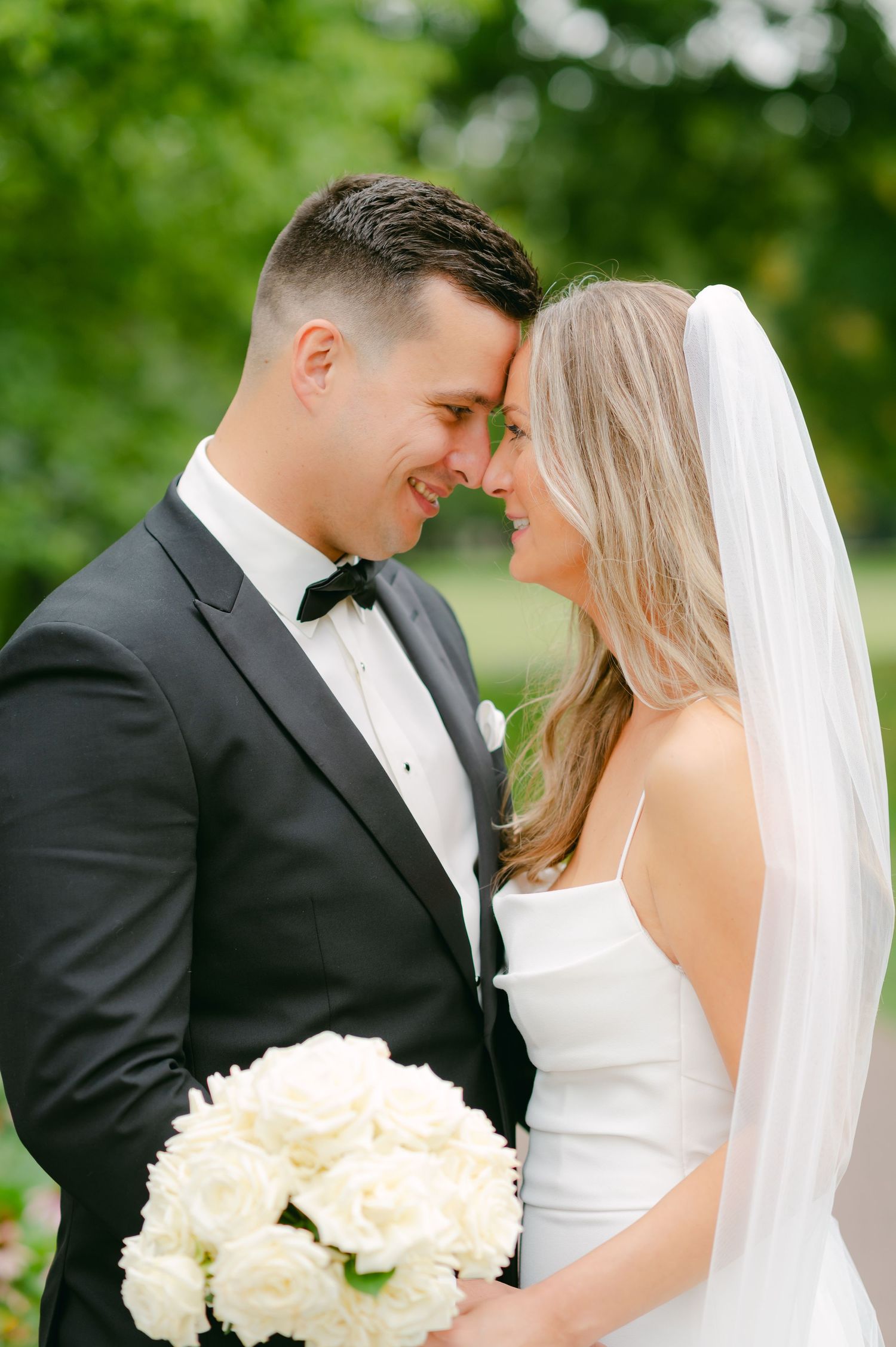 Romantic wedding portrait showing tender moment between couple with white roses in garden setting.