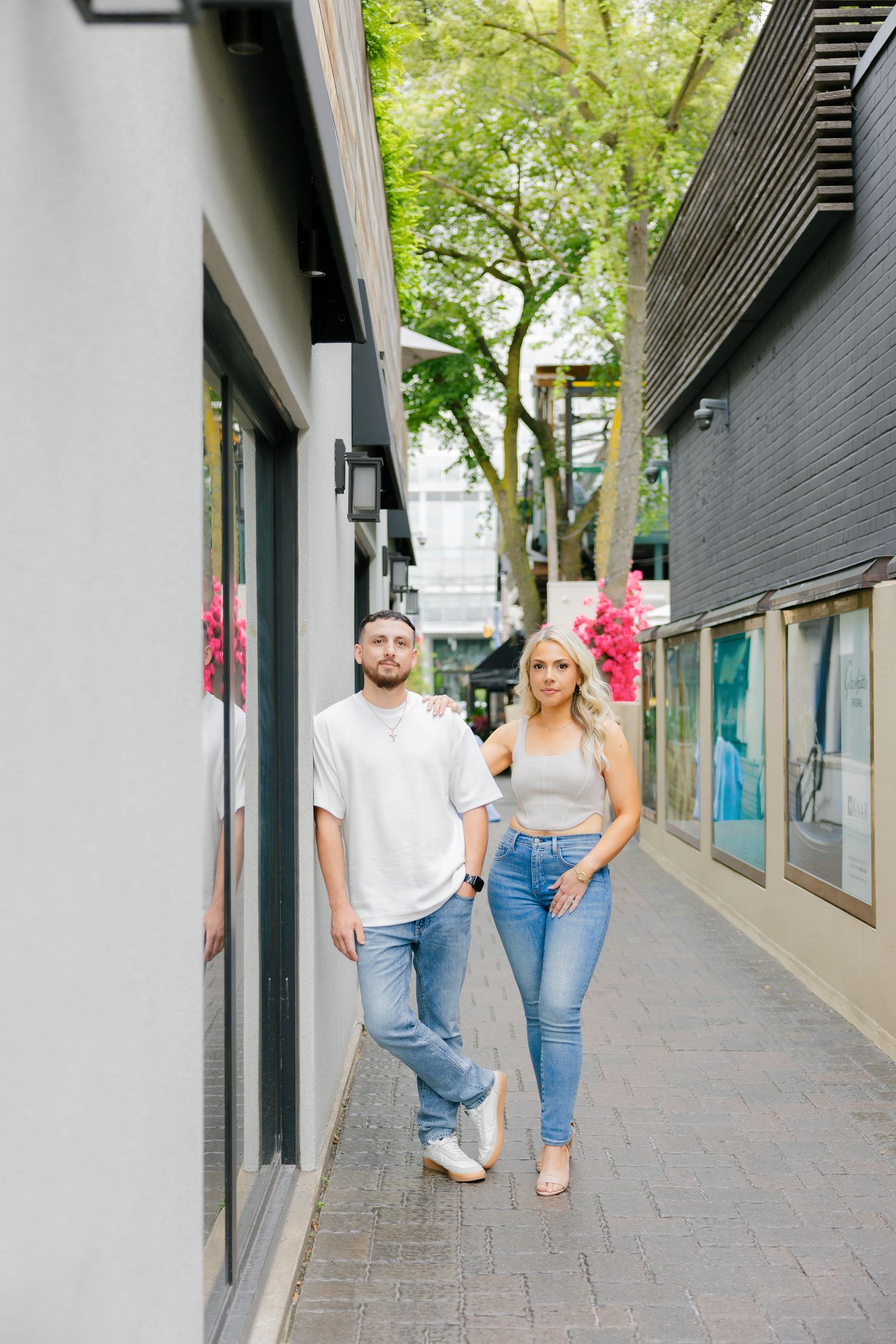 A relaxed couple in casual attire strolling down a tree-lined urban walkway.