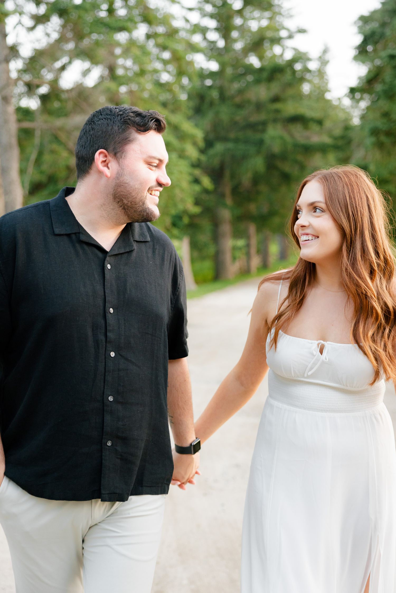 A happy couple shares a loving look while walking on a tree-lined path.