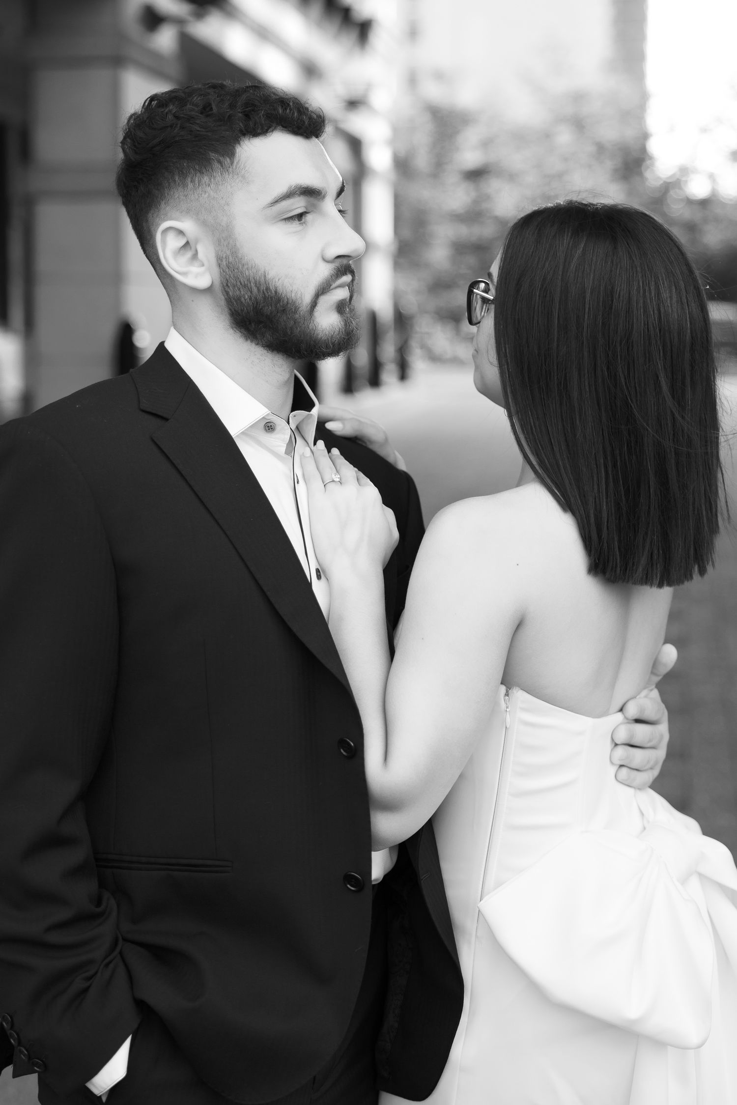 Intimate black and white portrait of a couple in formal attire against a city backdrop.