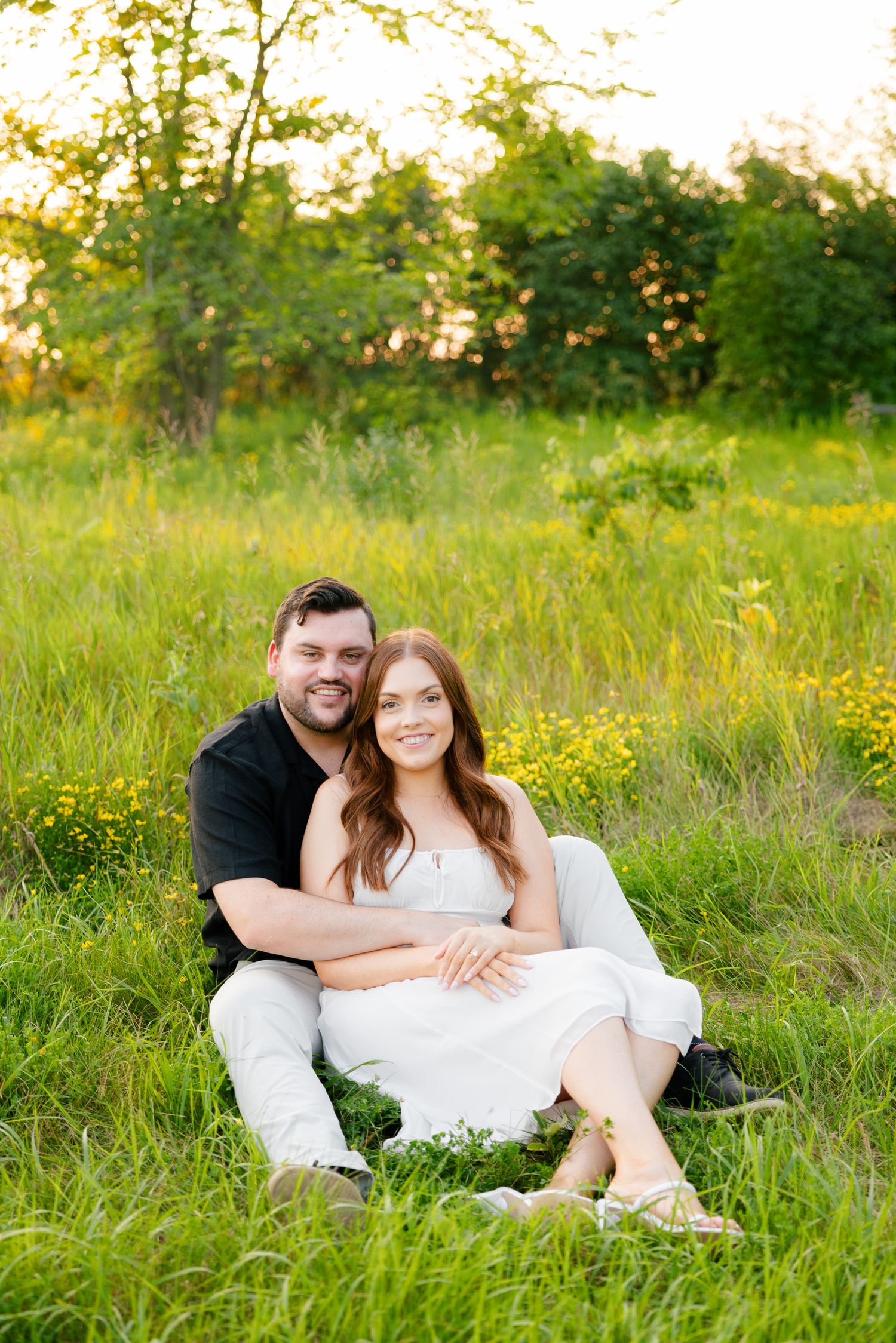 Couple relaxes together on grass surrounded by yellow wildflowers.