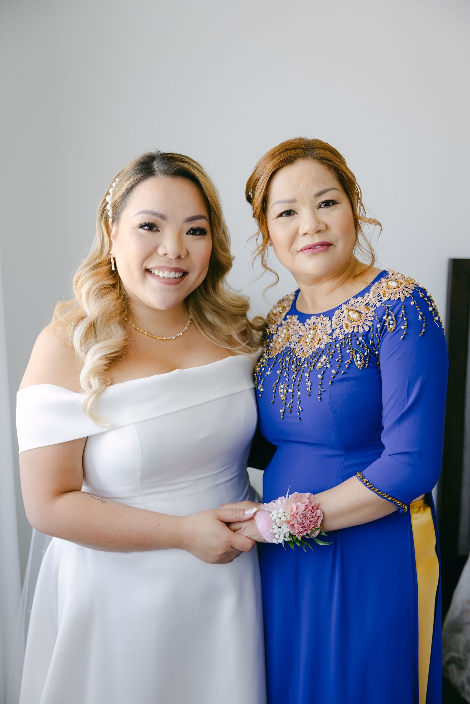 Bride in white dress poses with woman in embellished blue formal gown.