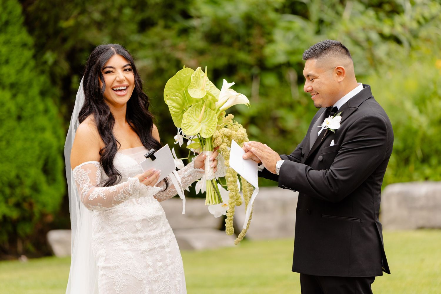 A joyful couple dances together in a garden setting with sunlit trees and greenery in the background.
