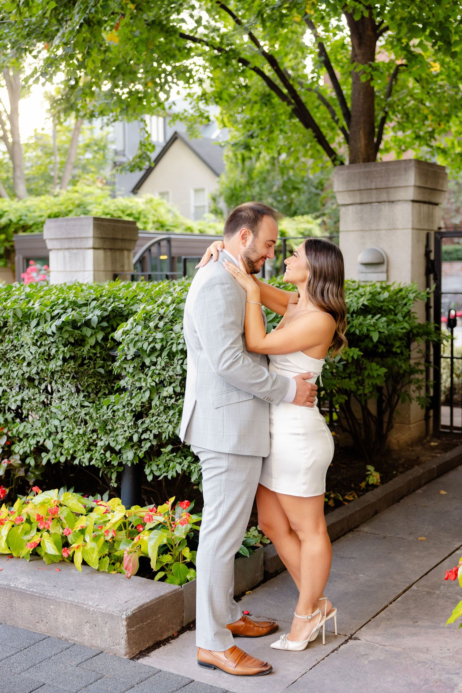 Couple sharing intimate moment against backdrop of manicured hedges and colorful flowers.