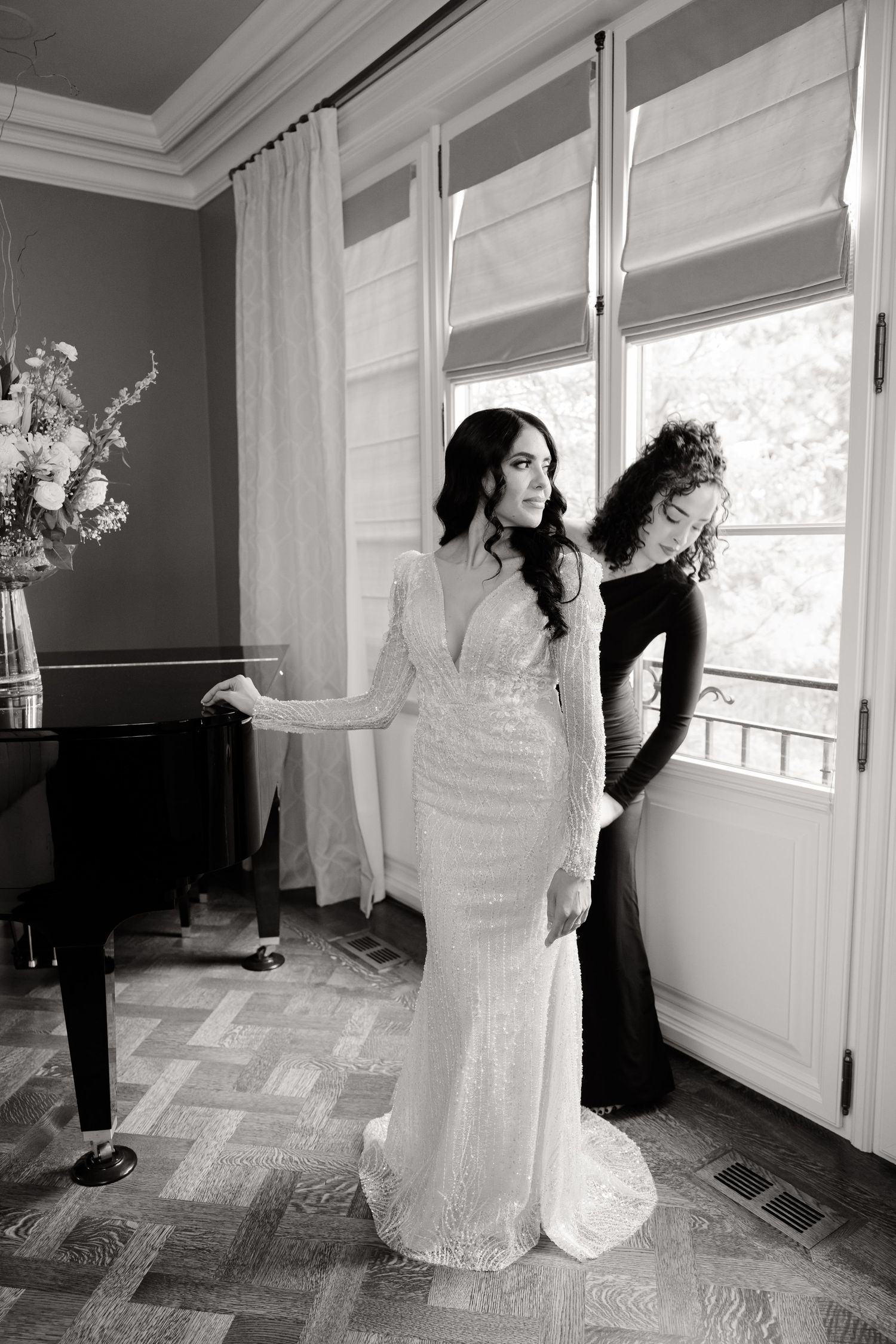Black and white photo of wedding dress fitting in elegant room with piano.
