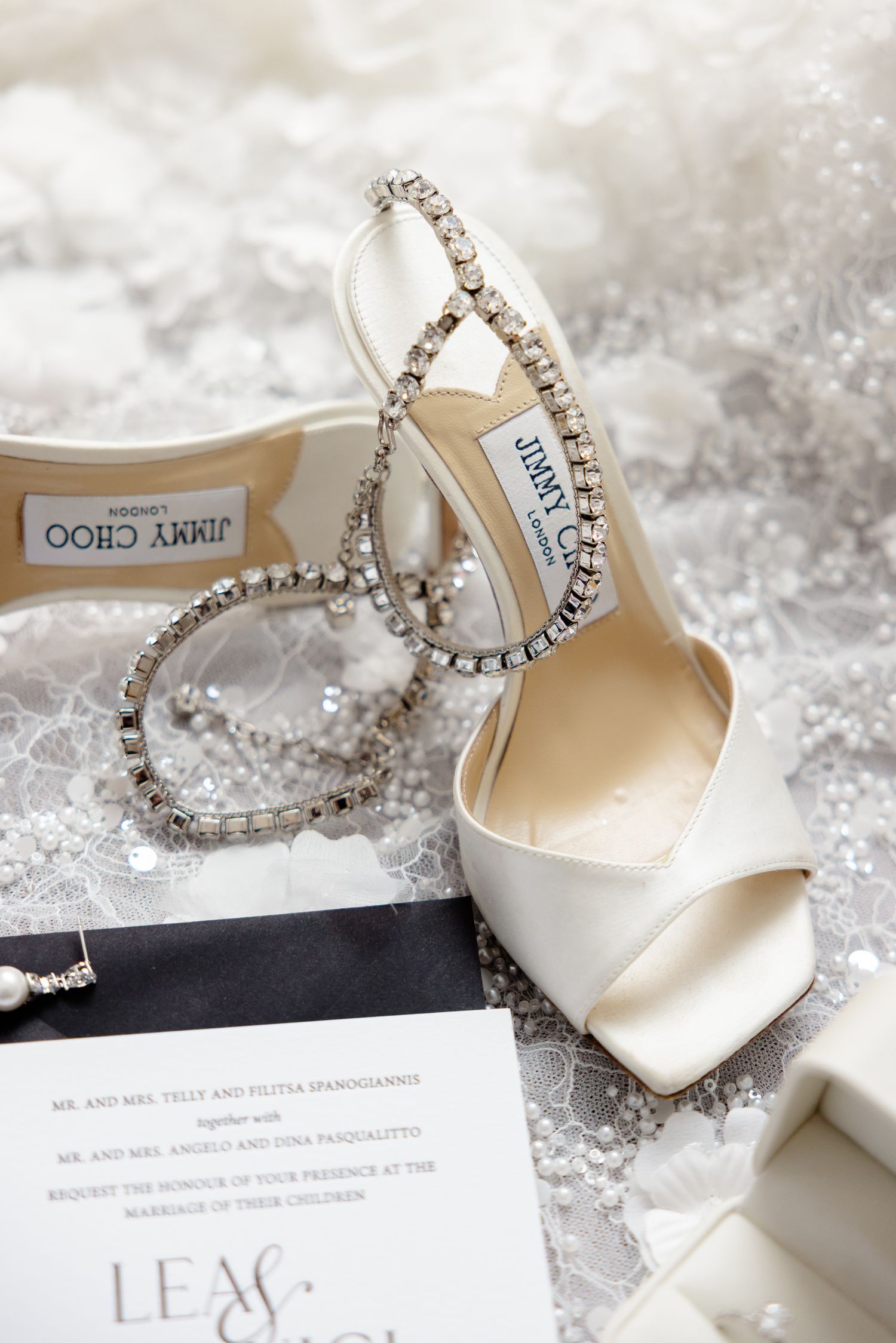 Elegant white Jimmy Choo bridal shoes with crystal embellishments and wedding stationery on a textured white surface.