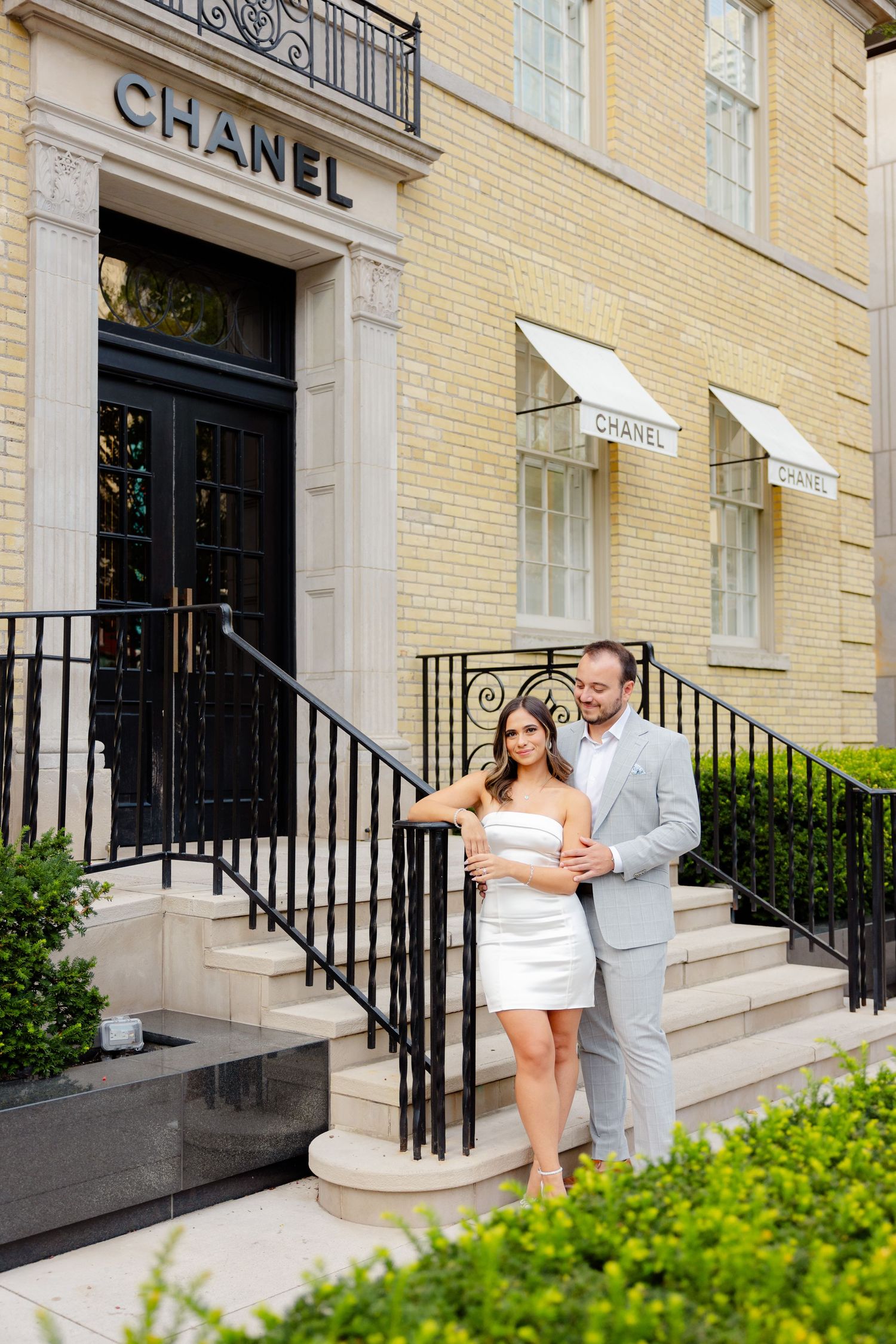 Elegant couple embraces on stone steps outside upscale Chanel boutique storefront.