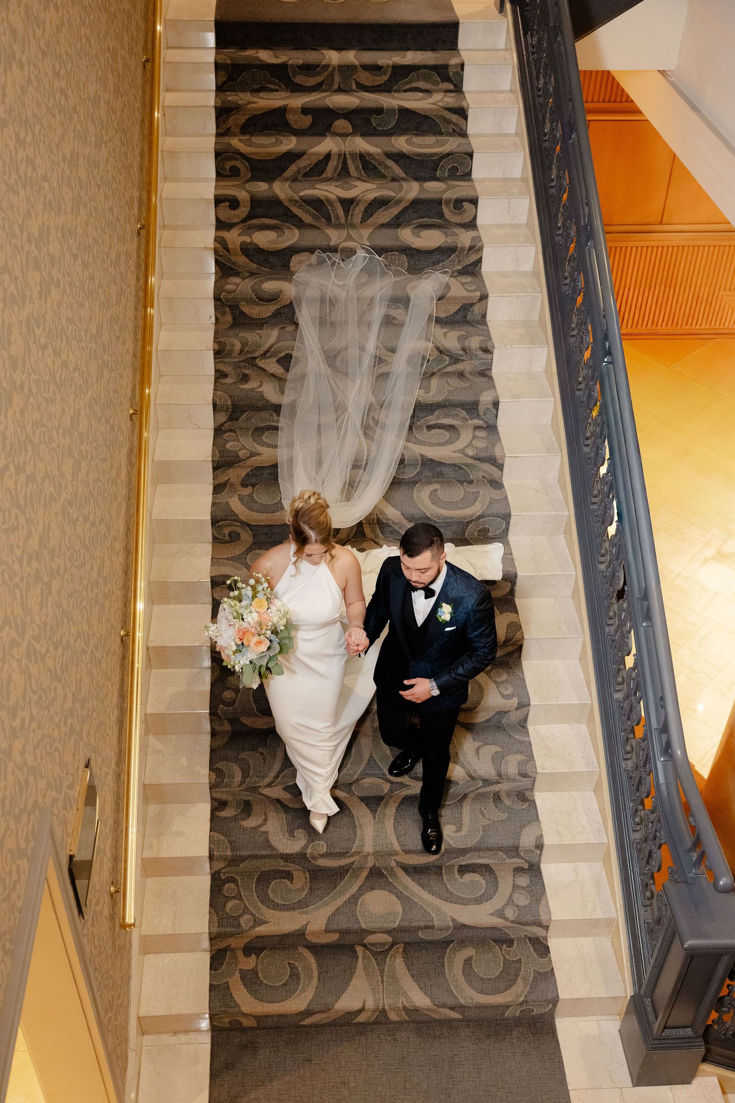 A bird's eye view of a couple descending an ornate staircase during their wedding celebration.