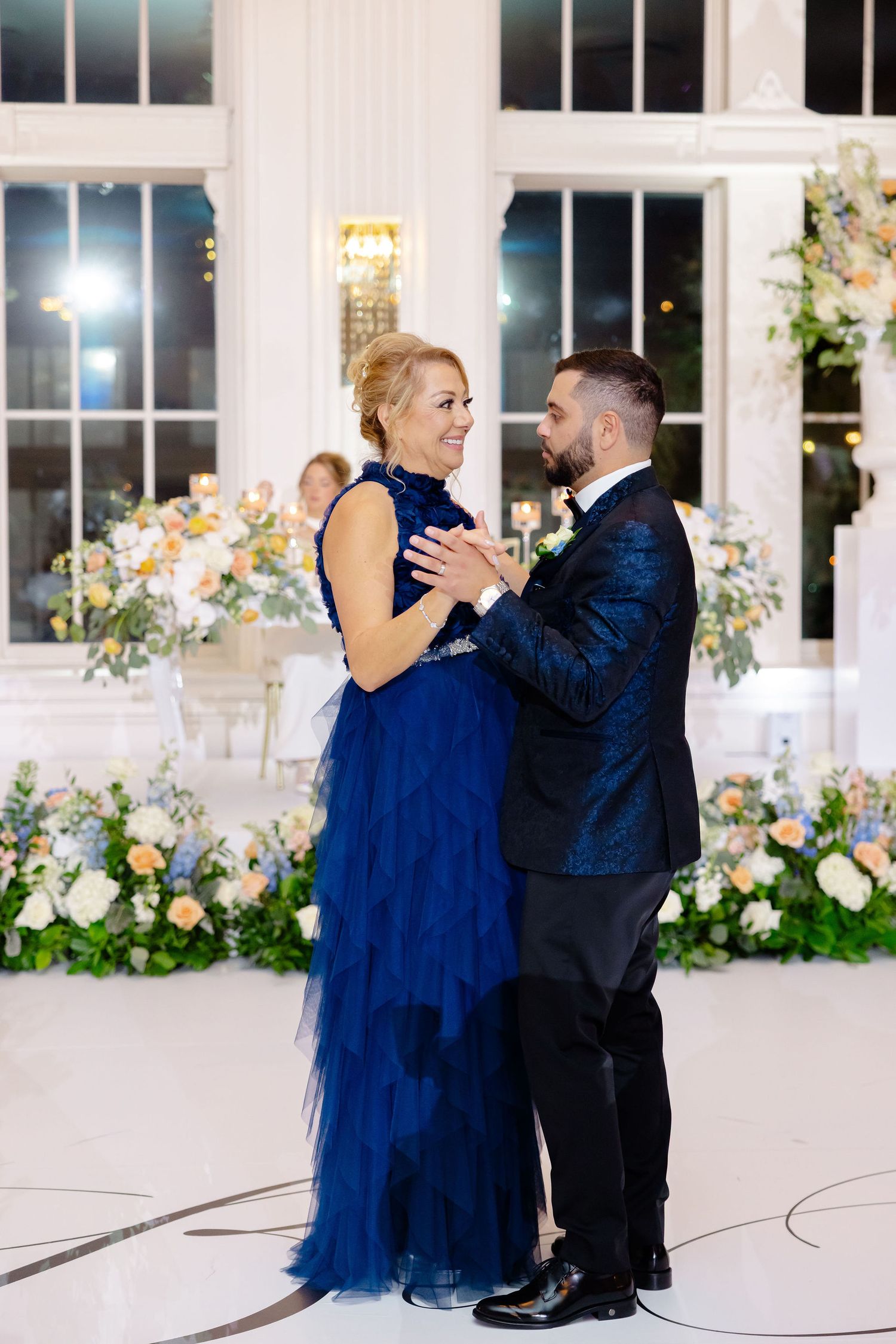 Couple sharing a romantic dance moment in a beautifully decorated white ballroom with floral decor.