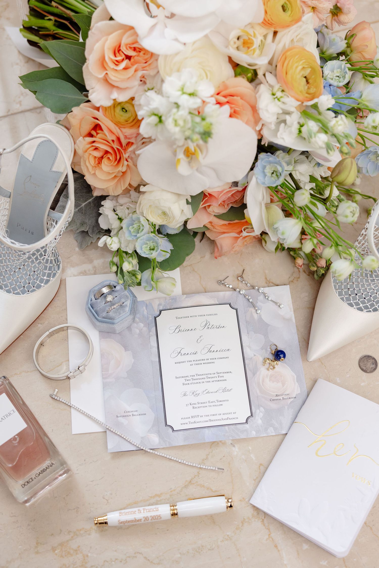 Elegant wedding stationery with peach roses and white flowers arranged on a marble surface with a gold pen.