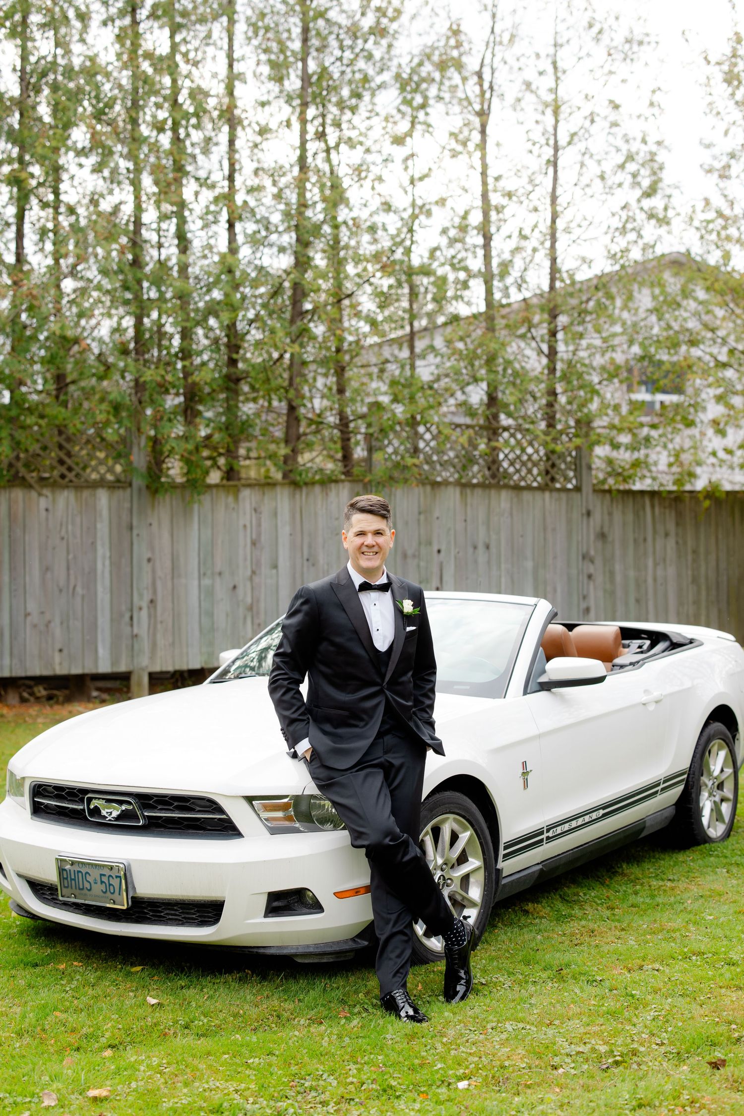 A white Ford Mustang convertible serves as backdrop for formal wedding photography.