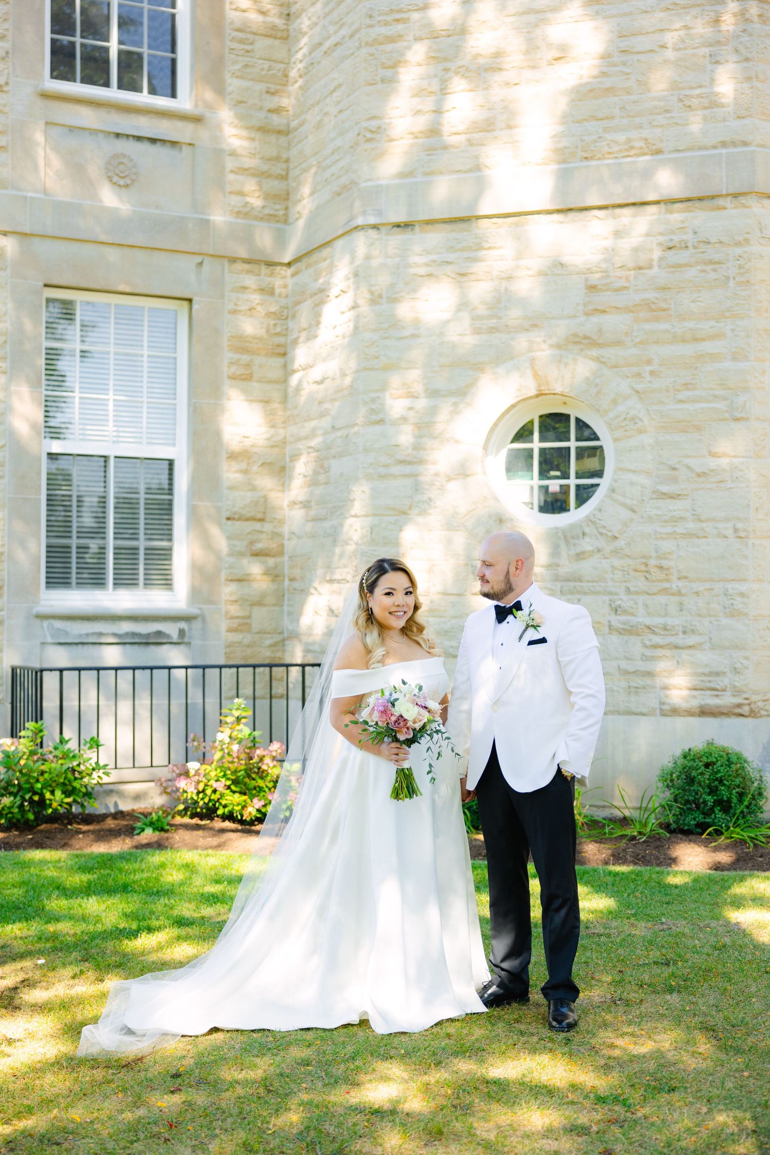 A summer wedding portrait with the couple standing before a classic stone facade.