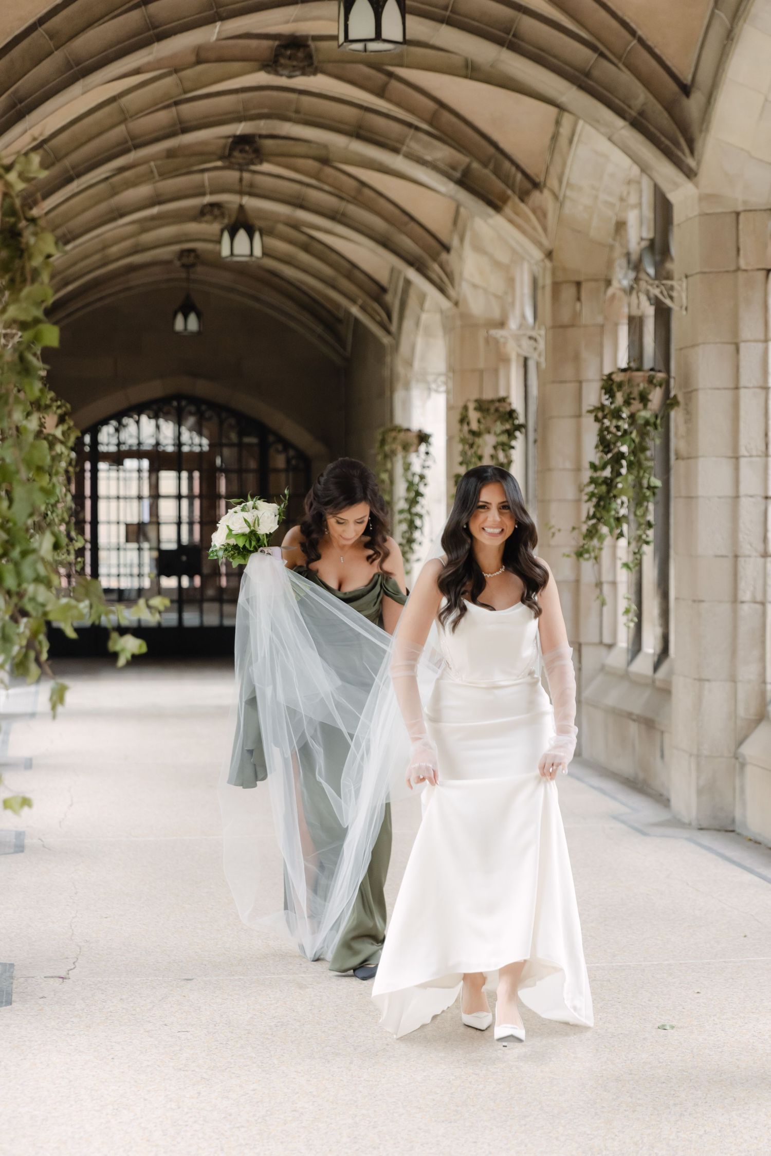 Two people walking through an ornate stone archway, one wearing an elegant white wedding gown.