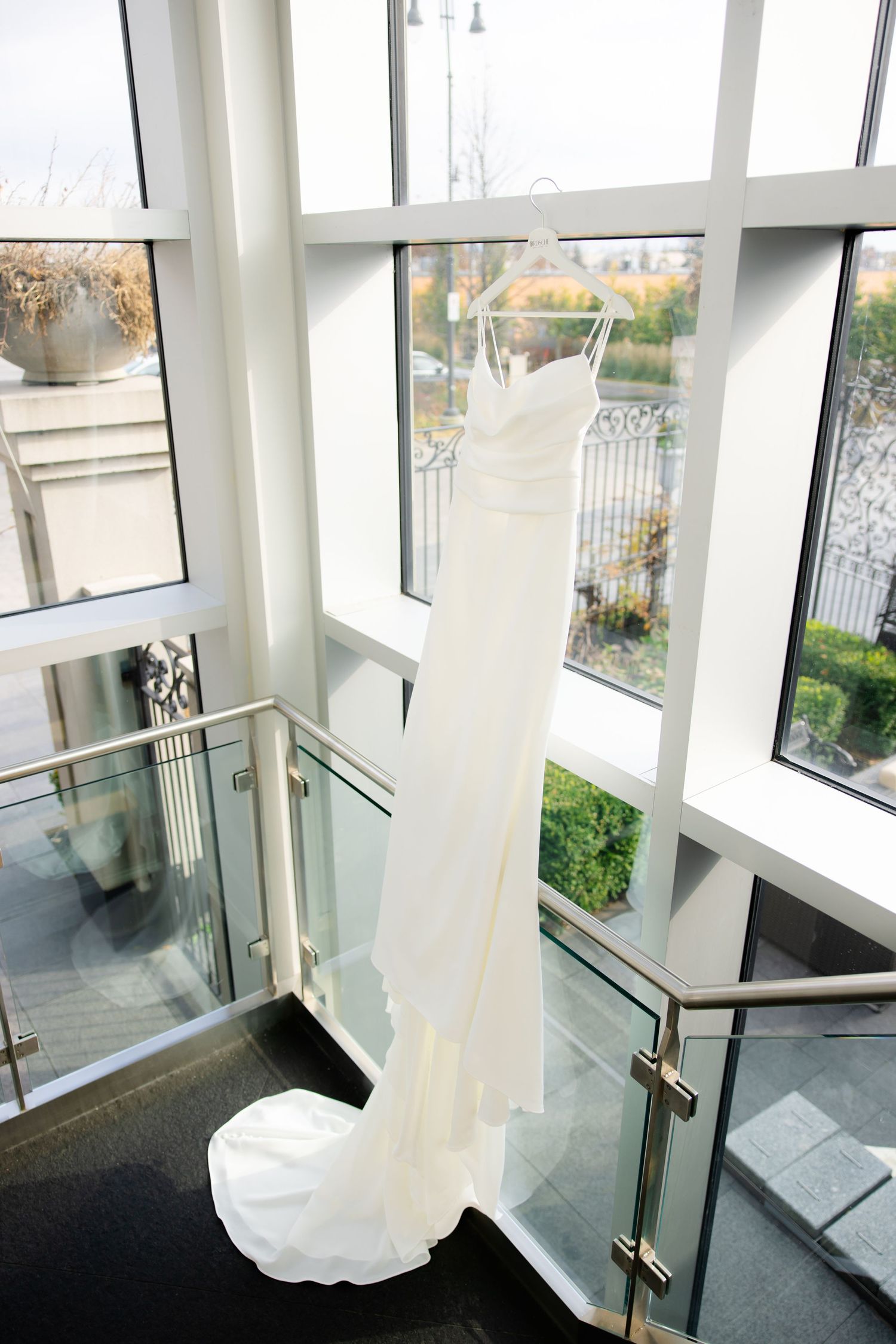 White wedding gown displayed against large windows in a modern architectural space.