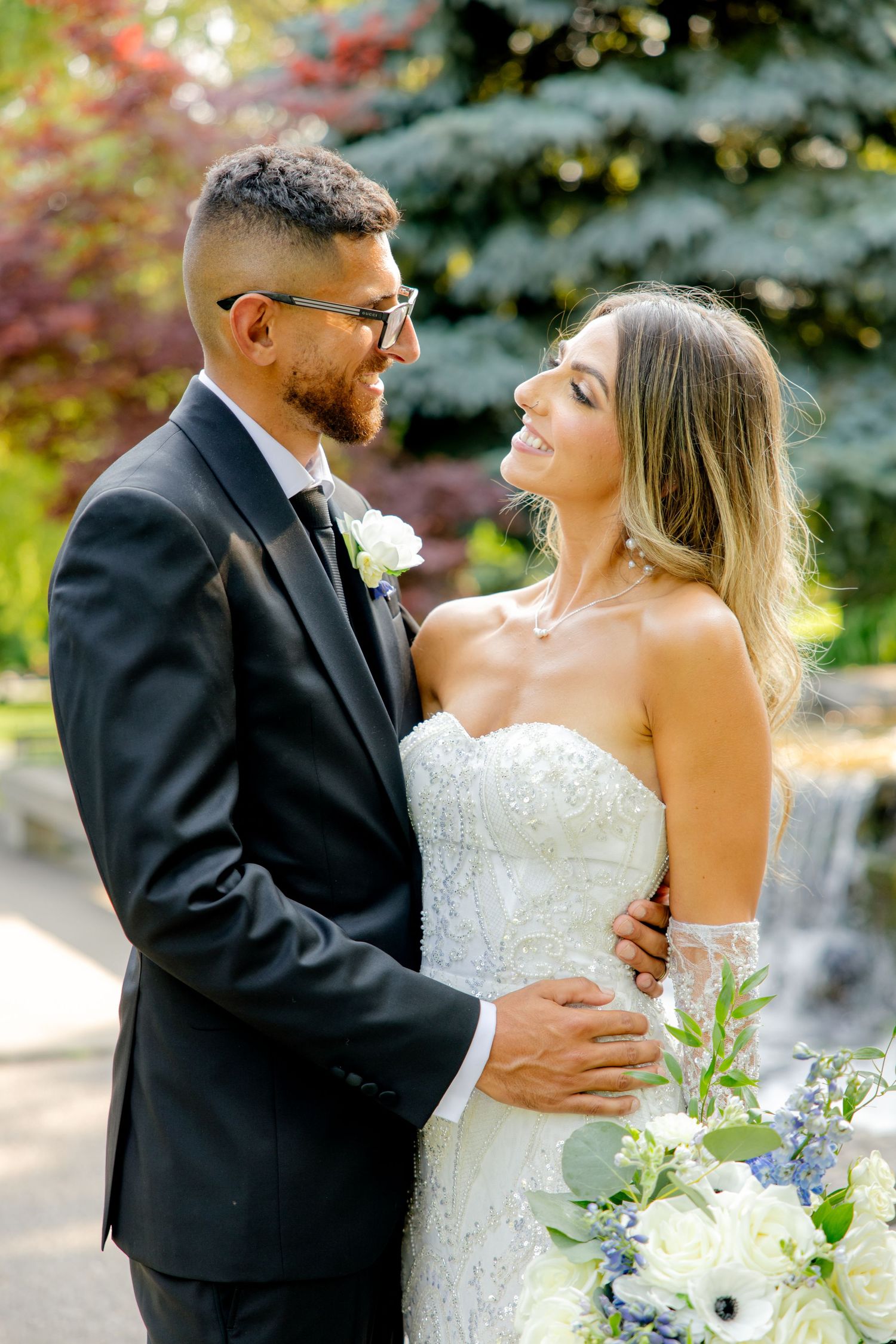 A romantic wedding portrait of a couple sharing a tender moment in front of a waterfall and blue spruce trees.