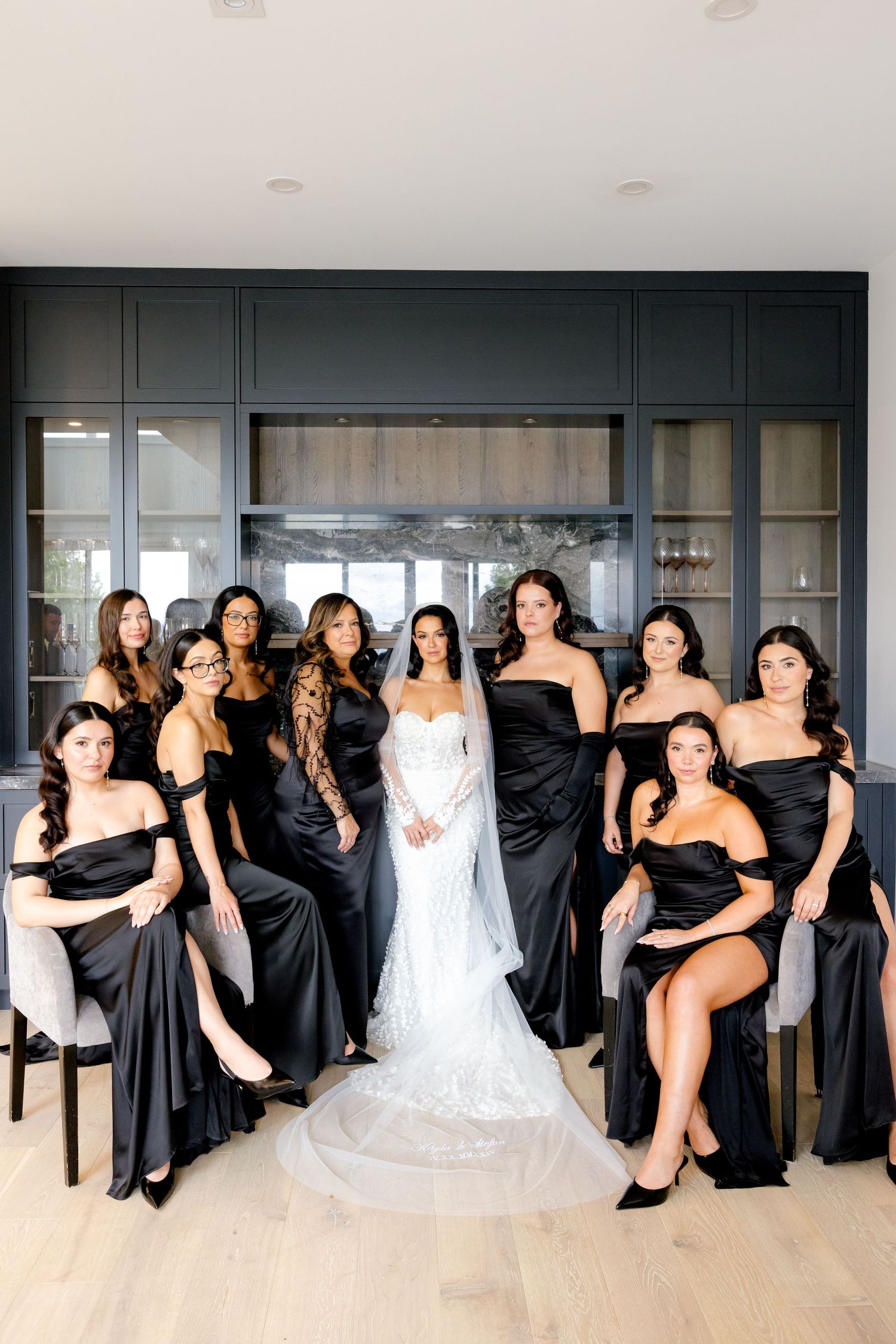 Glamorous bridal party seated and standing in modern space wearing coordinated black gowns.