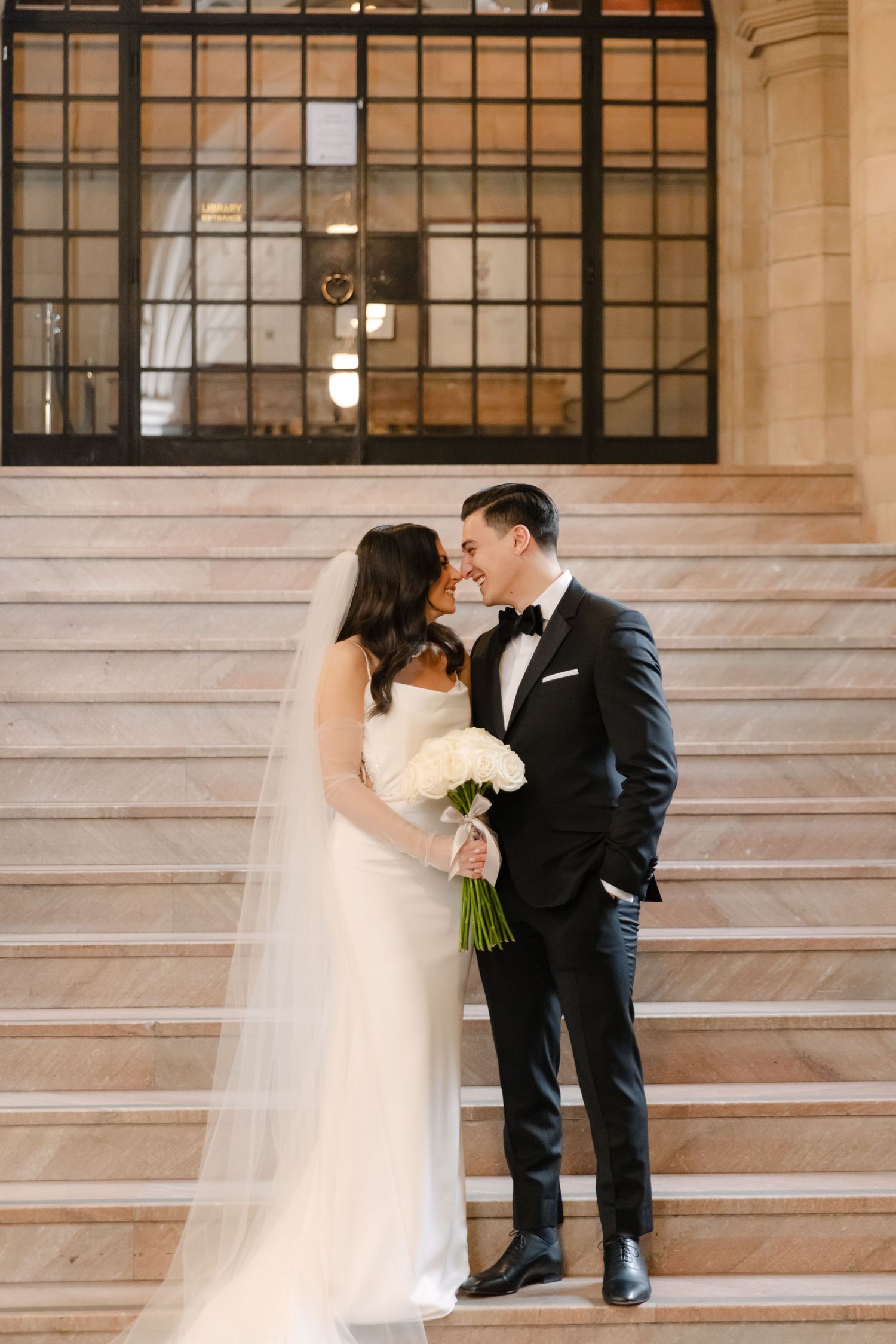 Formal portrait on classic stone steps with ornate iron window and architectural details.