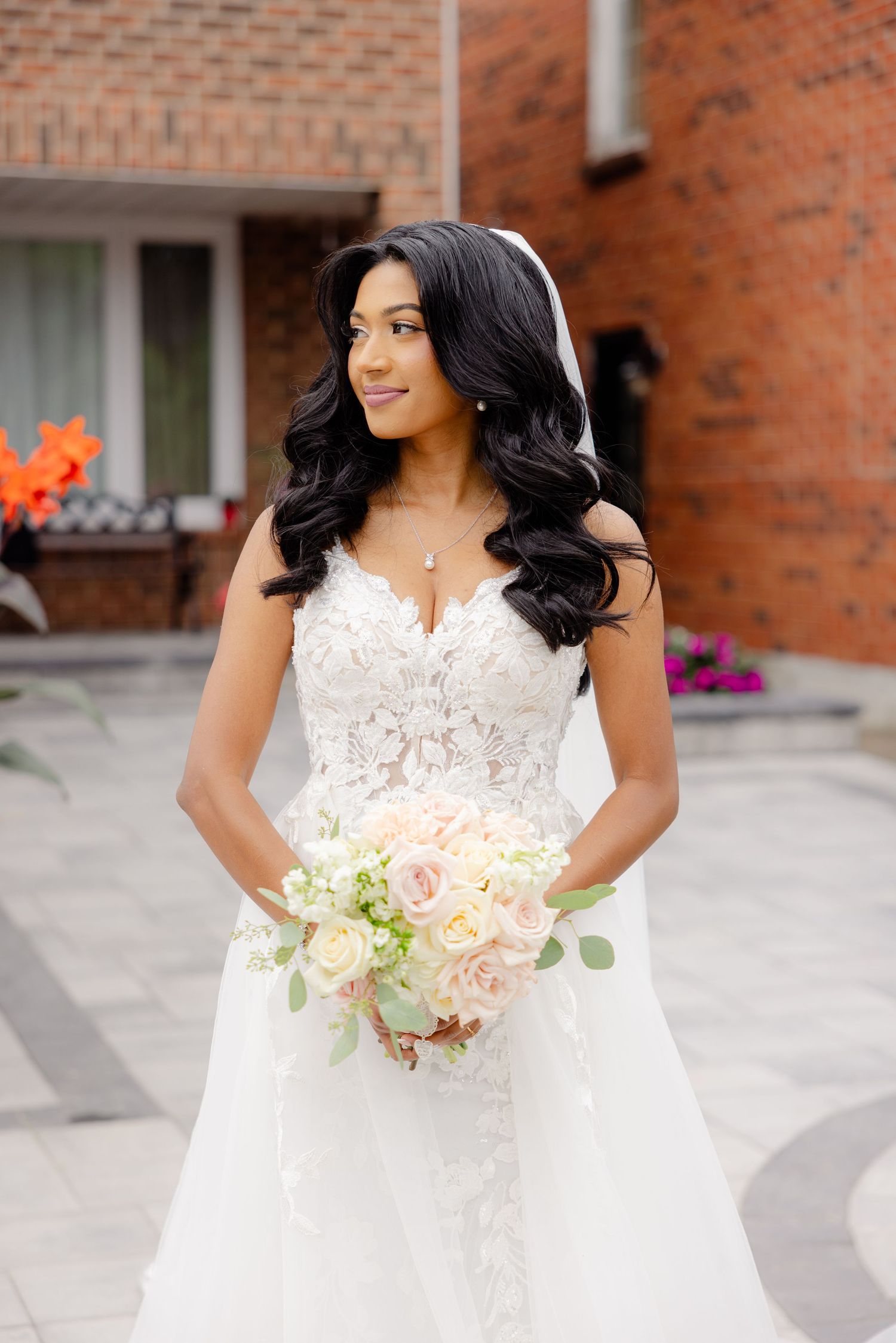 Close-up portrait of bride in detailed lace wedding dress holding delicate white and pink bouquet.