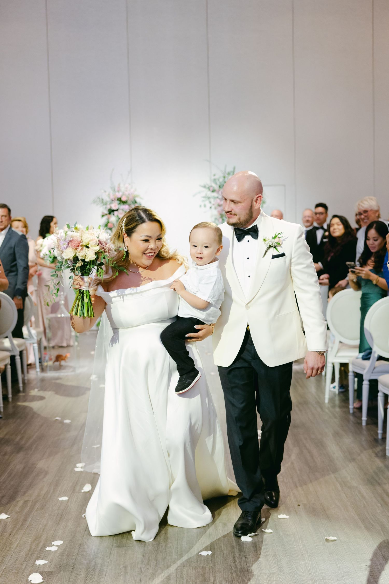 Happy wedding moment captured as couple carries child during ceremony recessional.