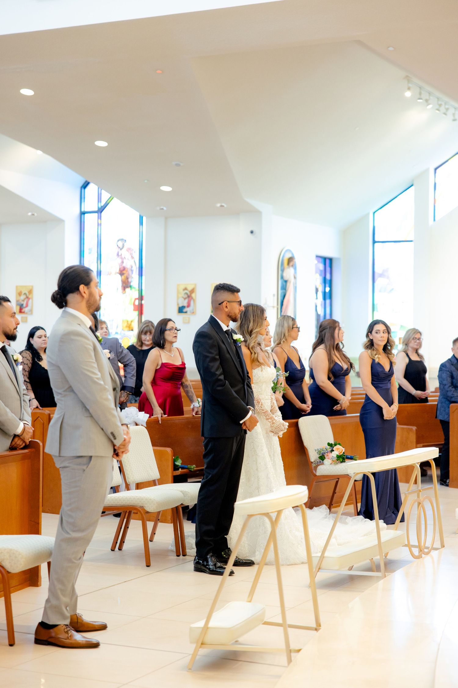 Wedding party standing in a modern church with blue stained glass windows and white walls.