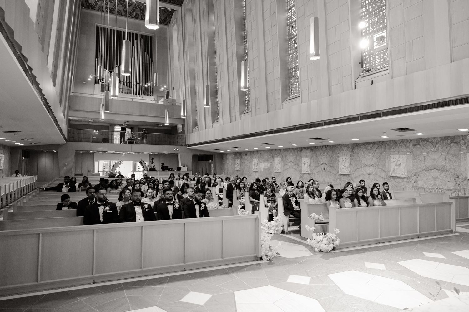 Black and white photo of wedding ceremony with guests seated in church pews.