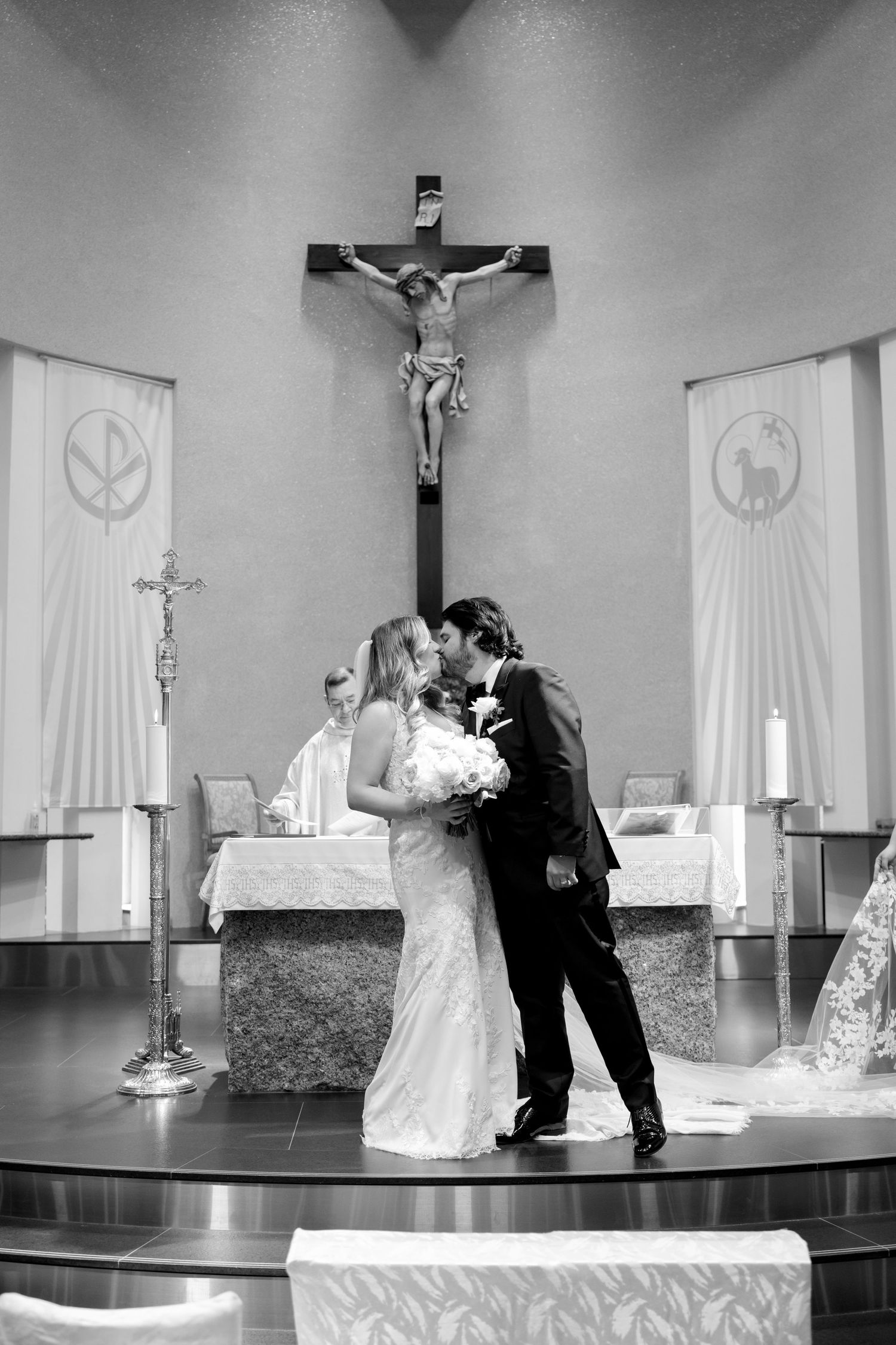Black and white photo of a romantic wedding ceremony moment at a church altar beneath a crucifix.
