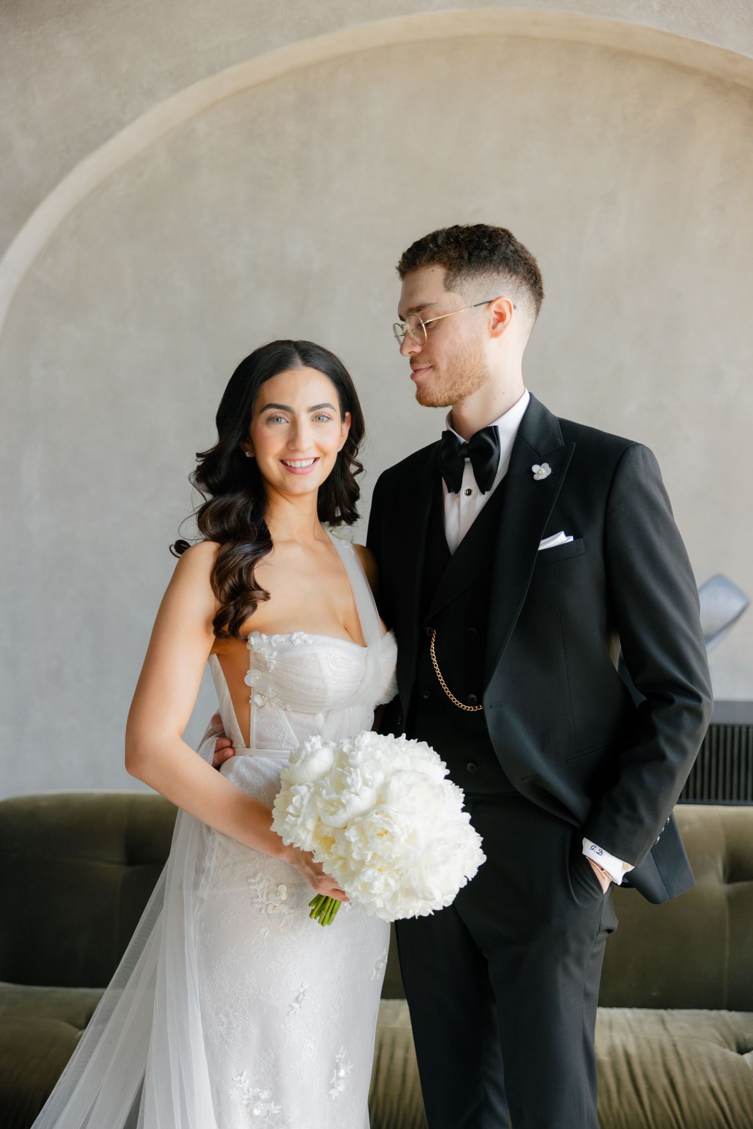 Intimate wedding portrait featuring couple with white bouquet against neutral backdrop.