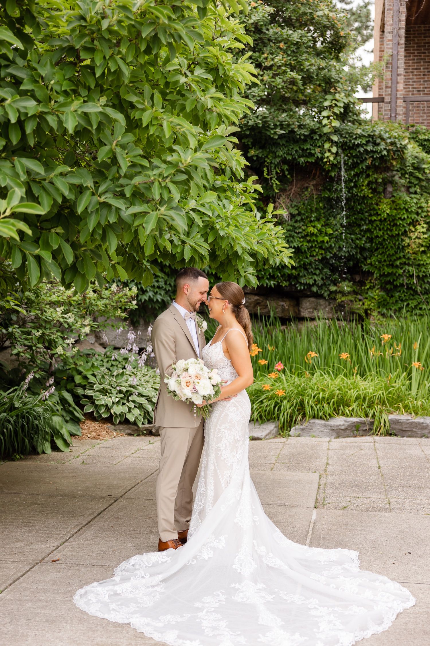 Romantic garden wedding photo with lace train flowing on stone pathway.