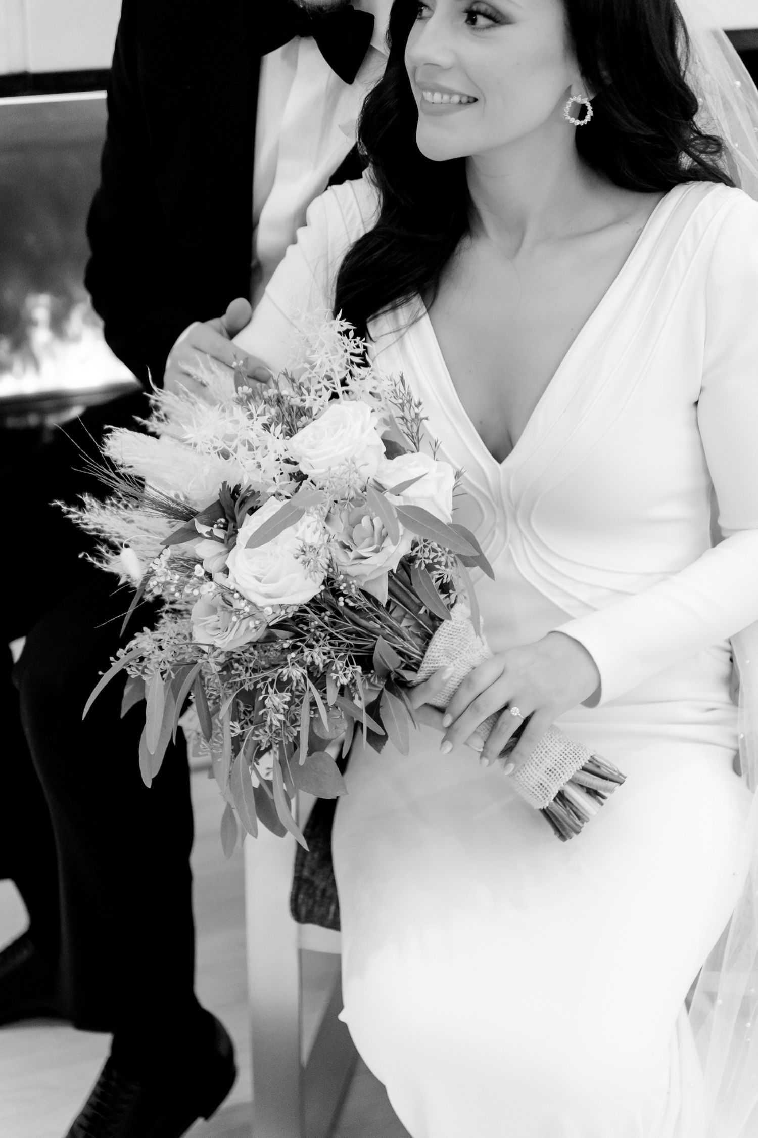 Elegant bride in white dress holds a lush bouquet of roses and greenery in black and white.