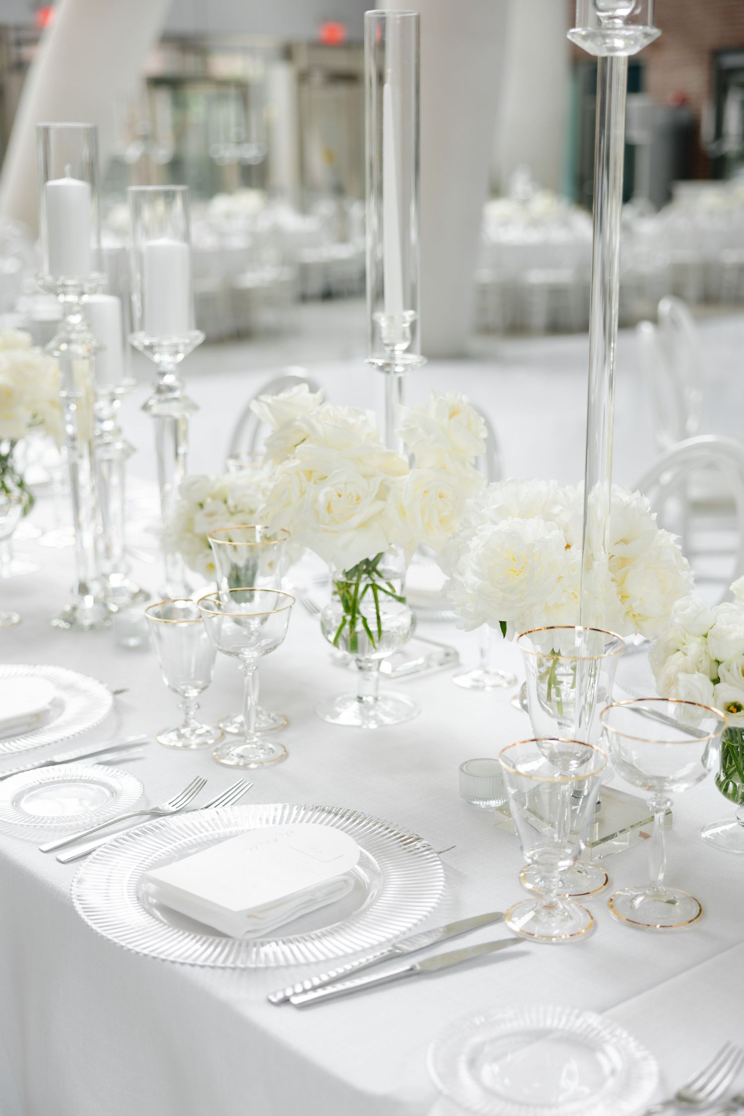Long dining table set with white linens, crystal glasses and white rose centerpieces for a formal event.