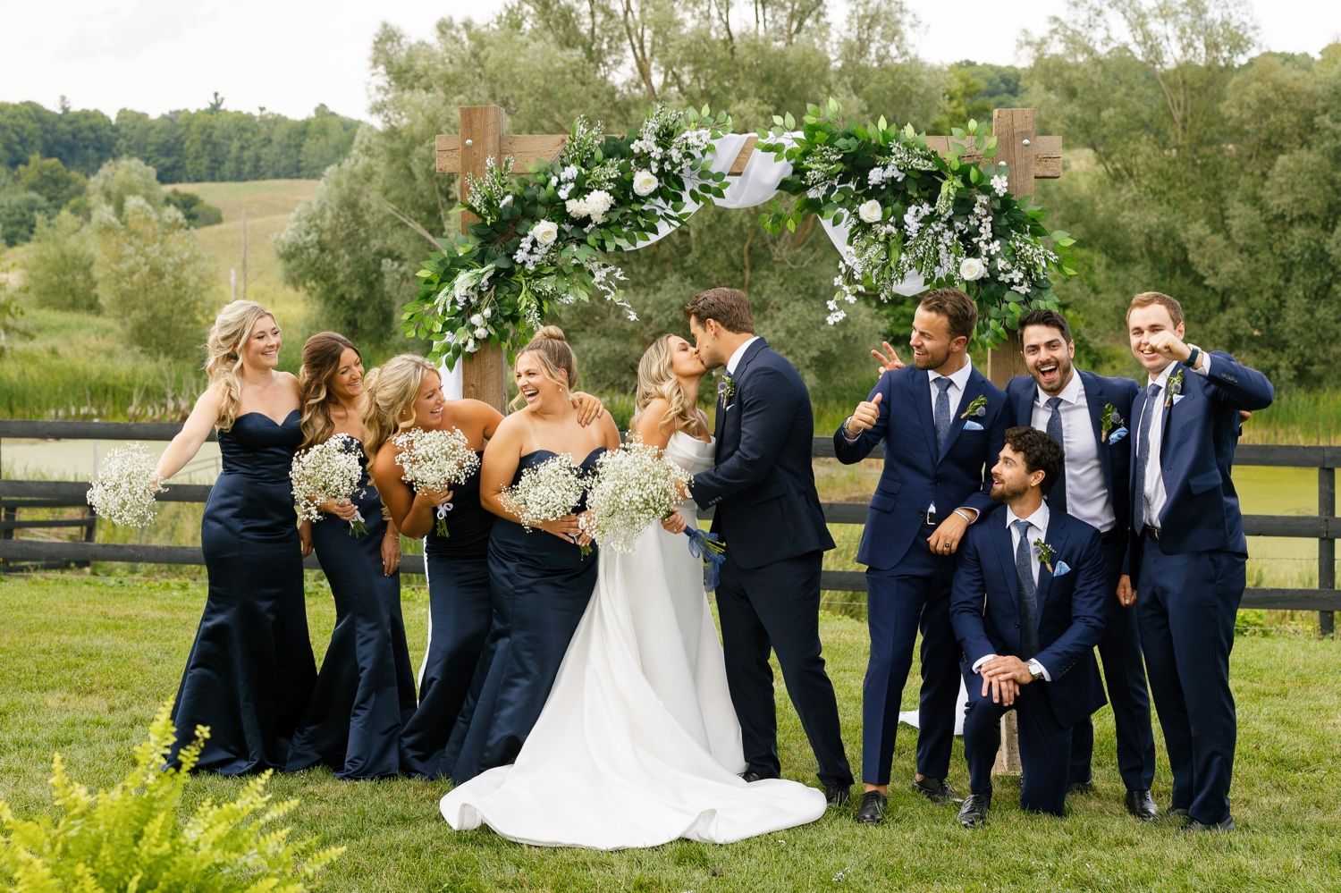 Wedding party showing personality with playful poses under decorated arch in garden setting.