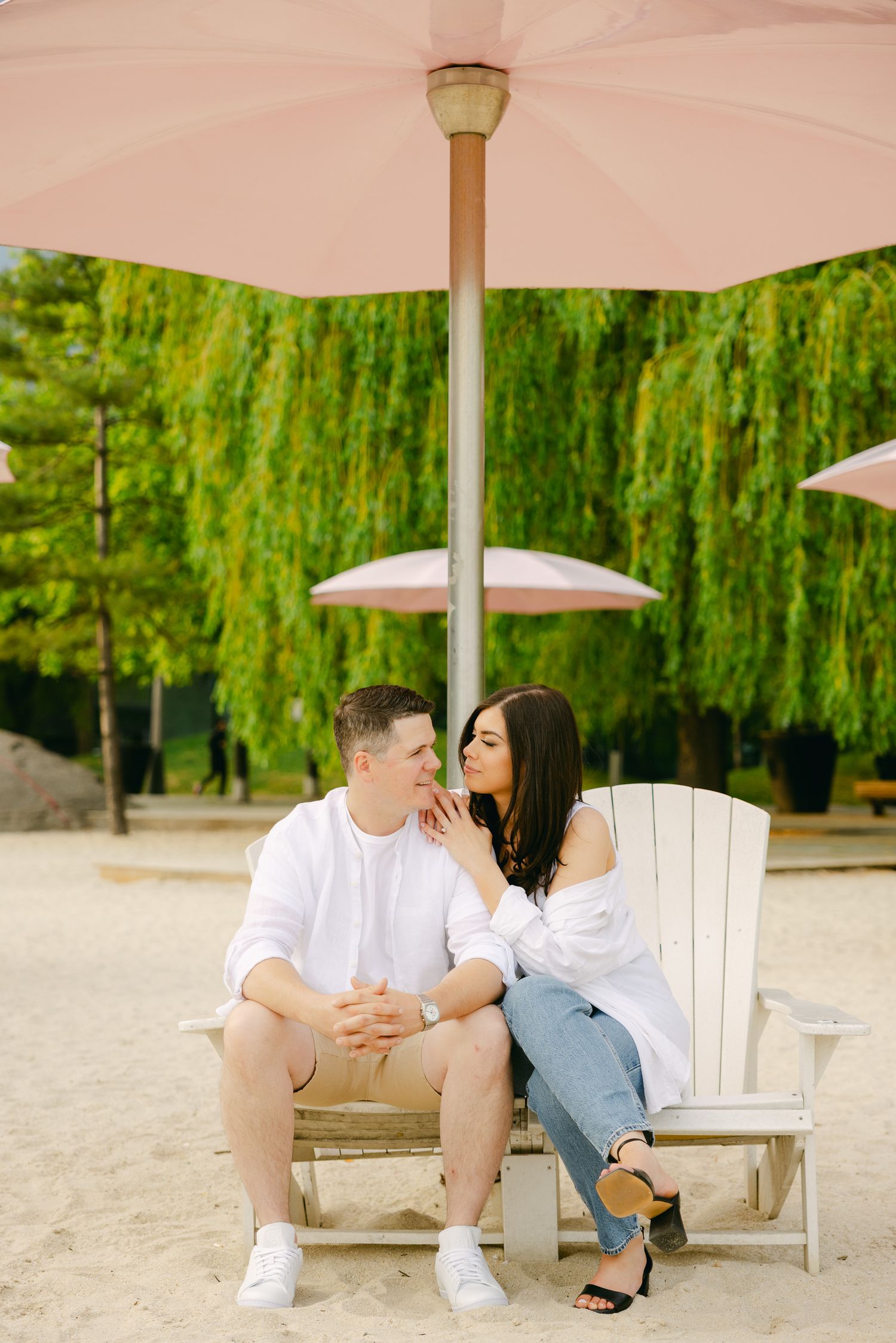 Intimate moment between couple on white Adirondack chair under pink umbrella.