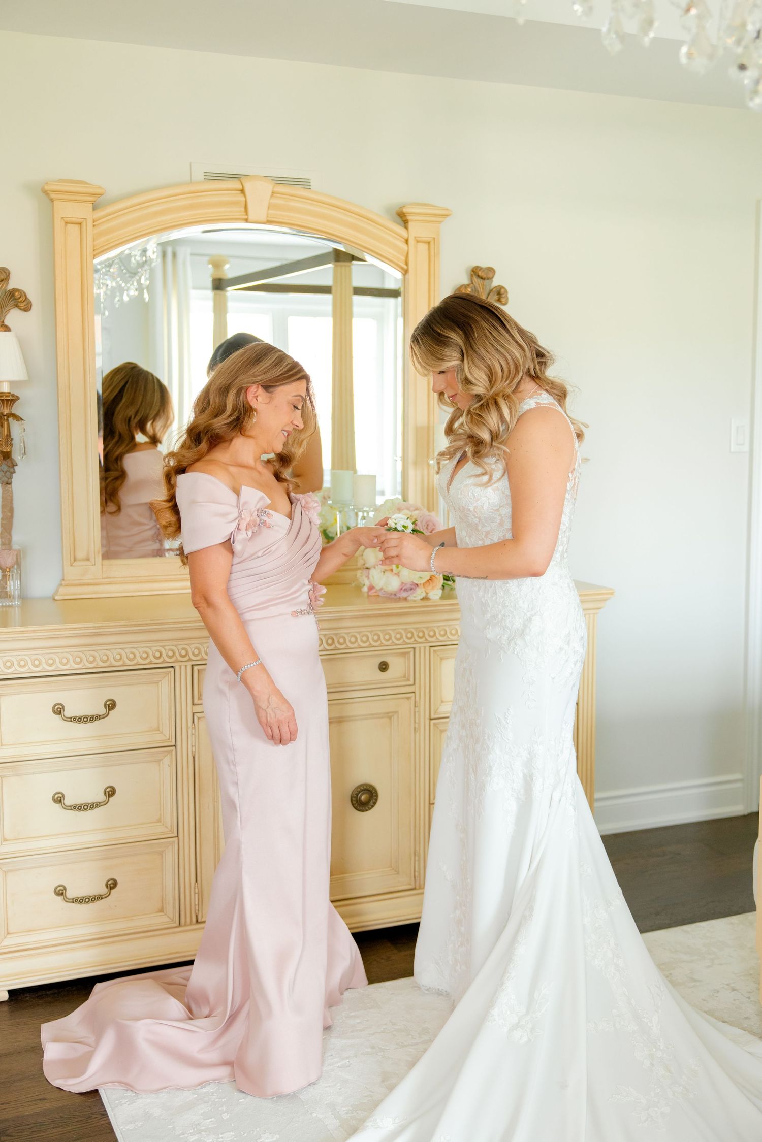 Intimate getting ready moment between two in pink and white gowns by vintage vanity.