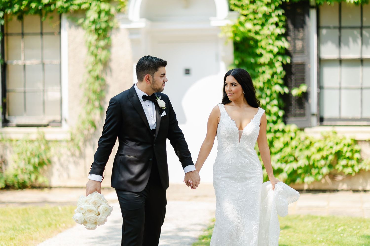 Happy newlyweds walk hand in hand along a path with lush greenery in the background.