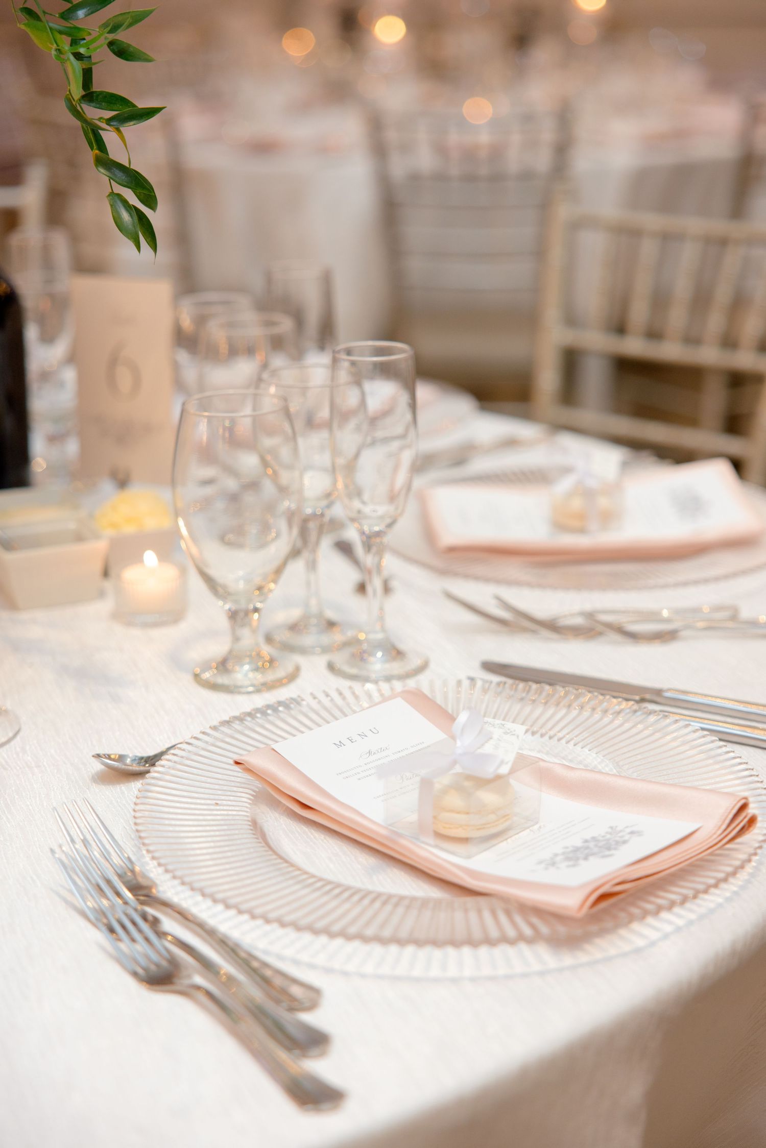 Elegant place setting with peach napkin, crystal glasses and white tablecloth at upscale wedding reception.