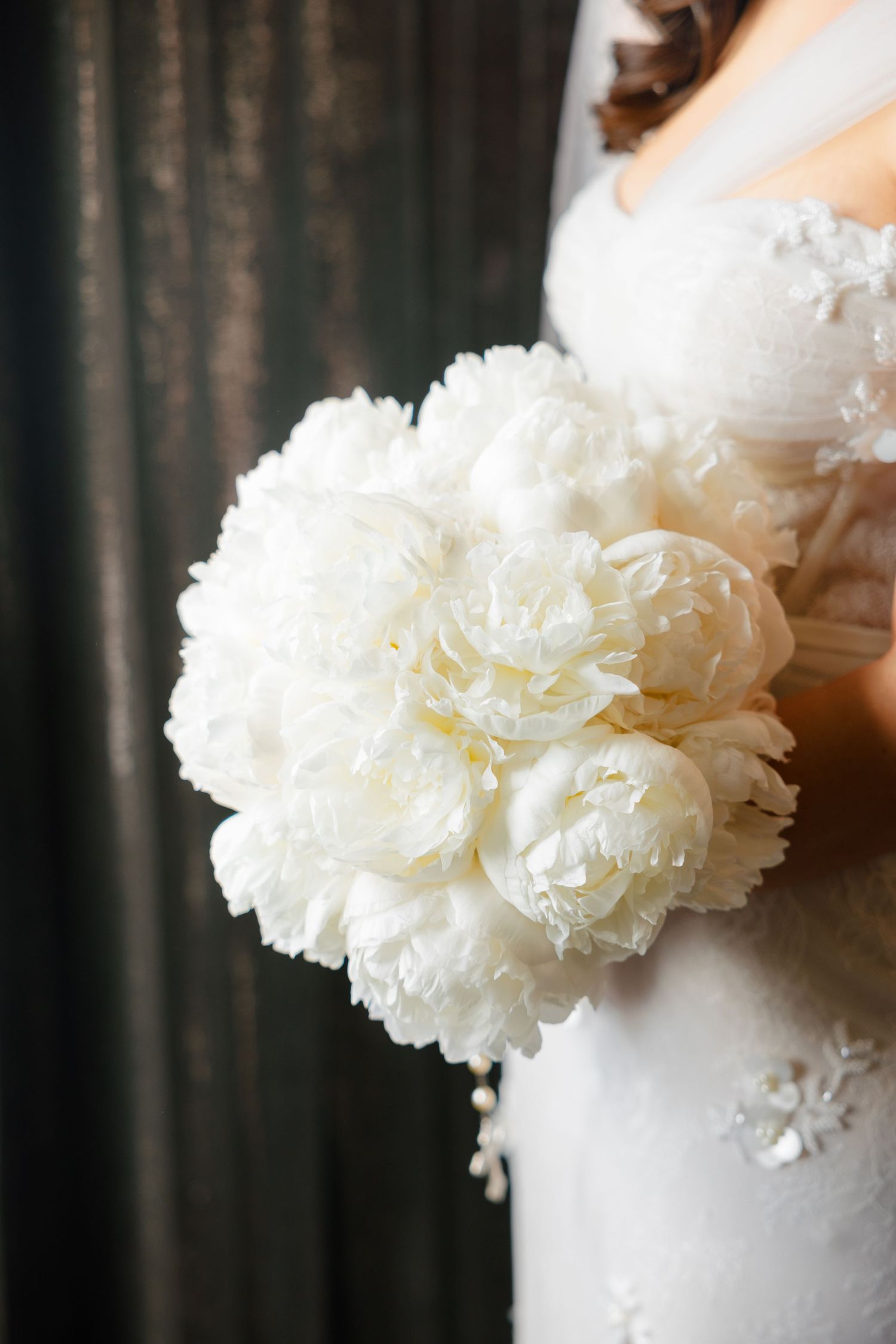 Detailed shot of lush white peony bridal bouquet against wedding dress.