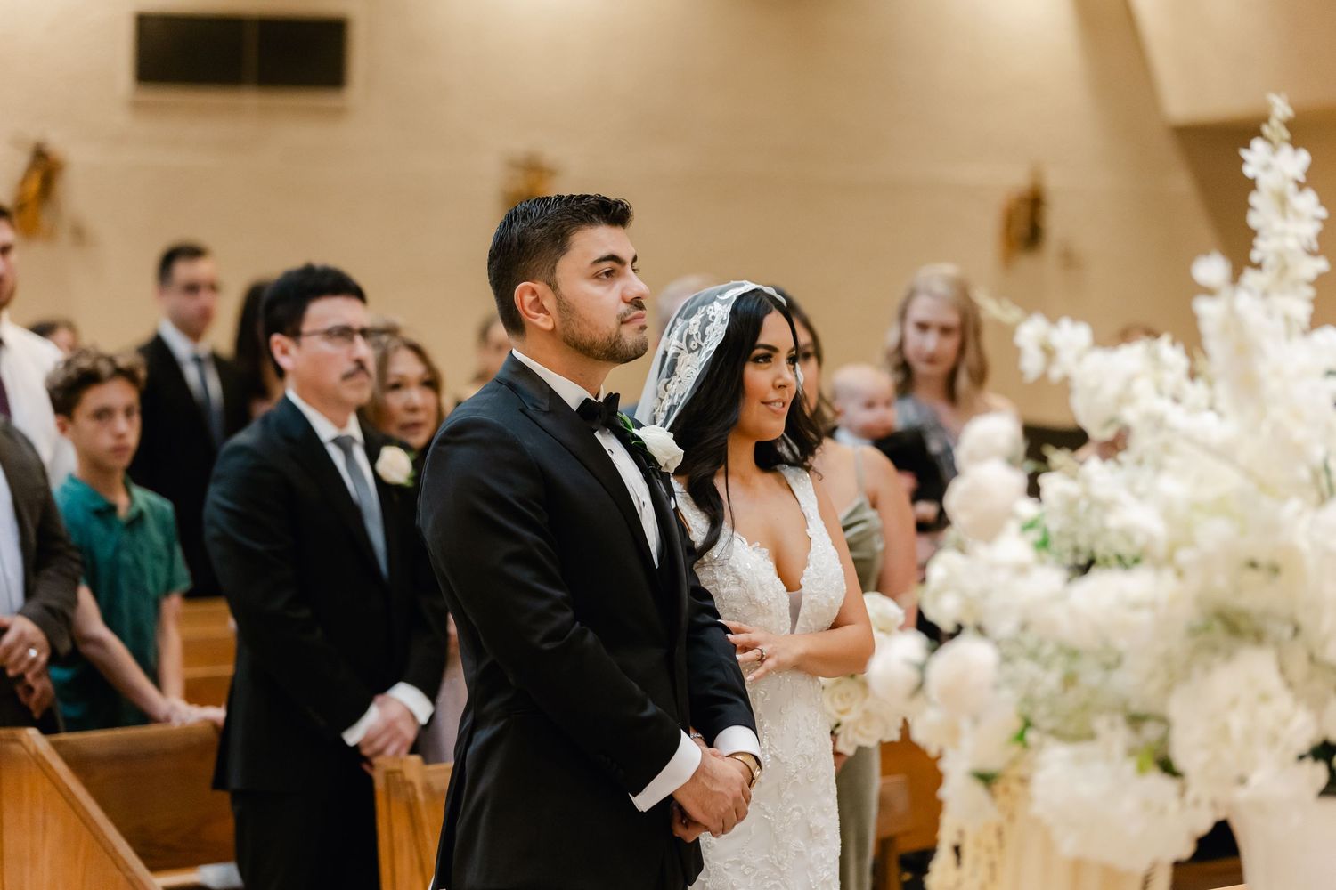 Wedding ceremony in church with white floral decorations and wooden pews.